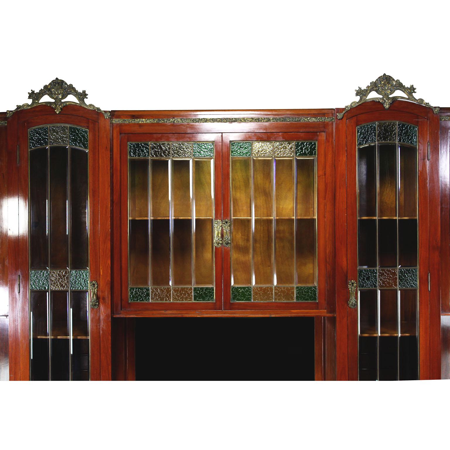 Una grande e imponente credenza-vetrina francese Art-Deco in mogano, legno satinato, vetro colorato e bronzo dorato. Il mobile alto con due ante a vetri superiori e centrali, affiancate da due ante alte e da una coppia di ante superiori a spigolo,