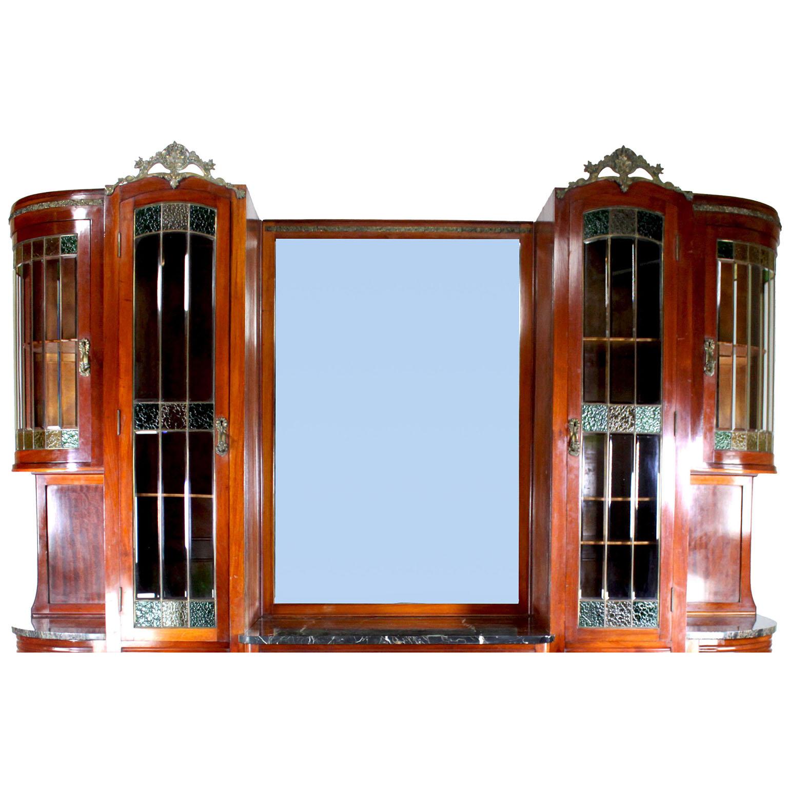 Una grande e imponente credenza-vetrina francese Art-Deco in mogano, legno satinato, vetro colorato e bronzo dorato. Il mobile alto ha una cornice centrale a specchio smussato, affiancata da due ante alte e da una coppia di ante superiori a spigolo,