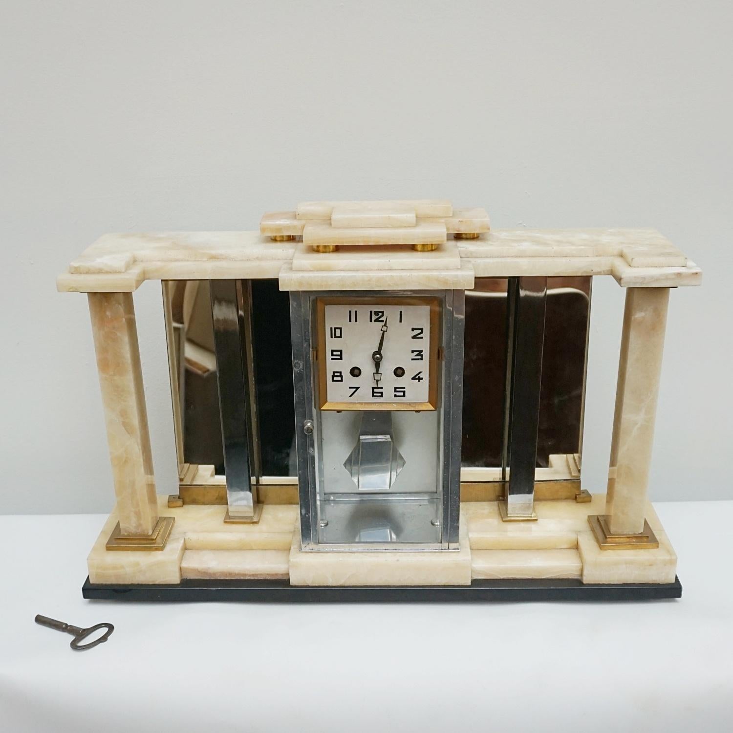 An Art Deco mantle clock. Marbled onyx on a black marble base with brass and chromed metal columns and a mirrored back inset. Brass cased clock face with Art Deco numerals.

Origin: French 

Date: circa, 1930.