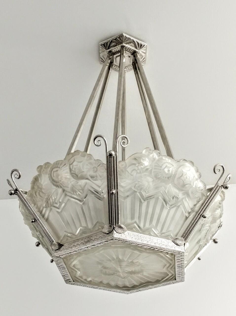 A French Art Deco chandelier by the French Artist Jean Noverdy. Six shades with matching hexagonal center coupe in clear frosted glass with intricate flowers with geometric motif details. Supported by a nickeled wrought iron frame. Chandelier has