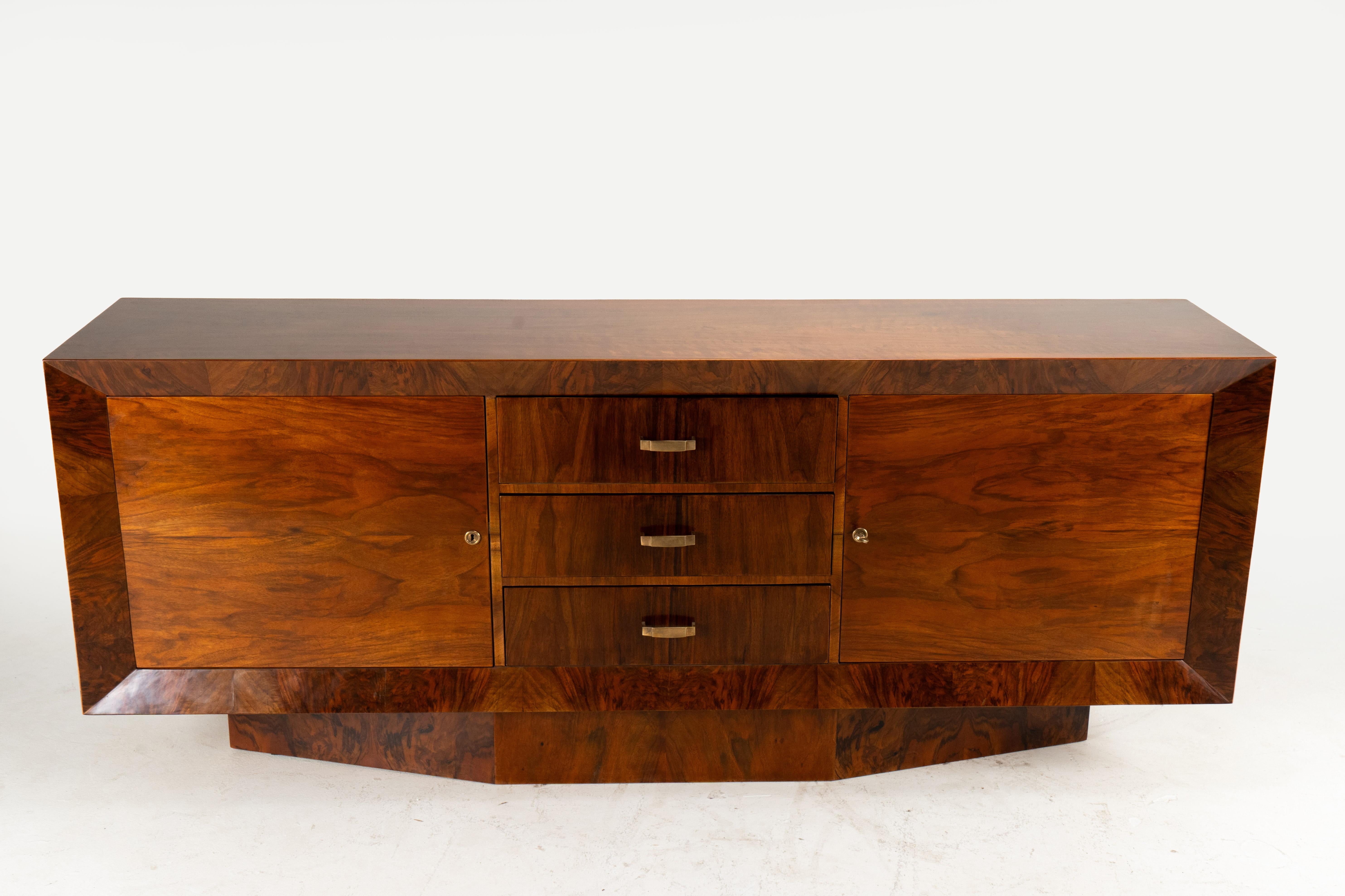 This is an exceptionally simple late Art Deco sideboard from France, c. 1940's. The piece features a sharply angled and deeply beveled front and base, with the walnut wood grain running vertically, like parquetry, in small sections. The doors are