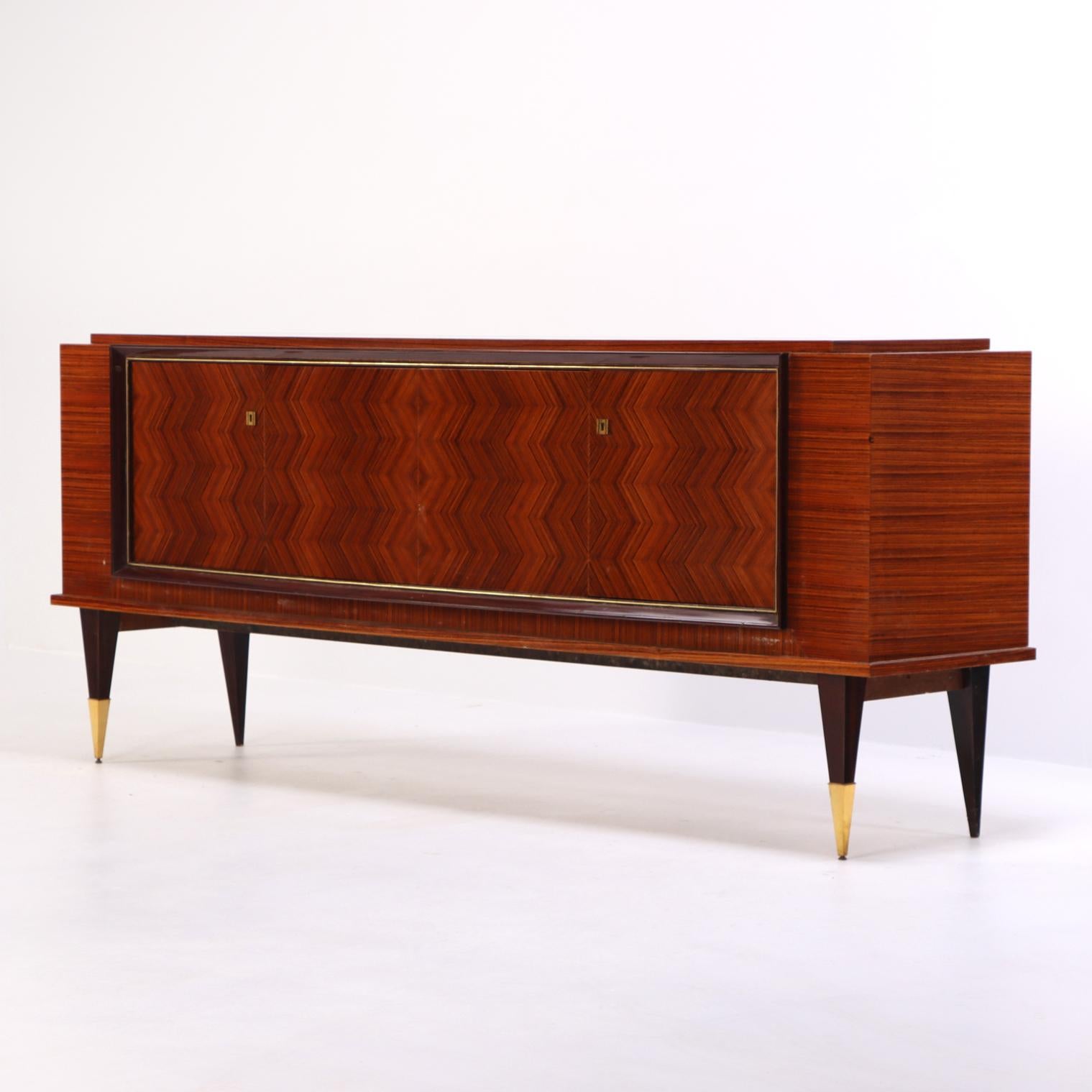 This striking sideboard showcases the streamlined elegance of French Art Deco design. Its exterior features rich, exotic wood veneers, beautifully highlighted by the geometric balance of four doors. The doors reveal 2 short shelves and 4 short