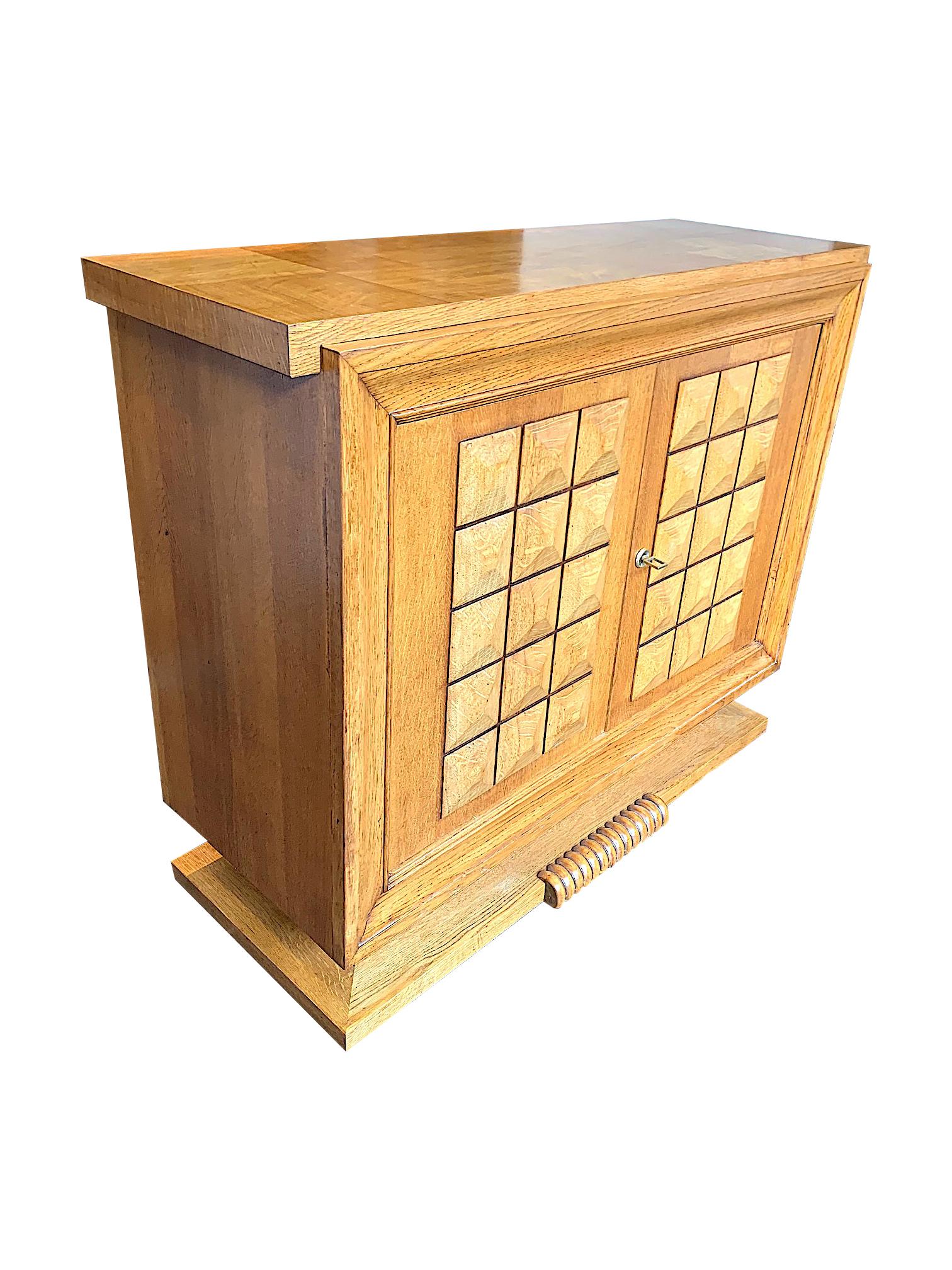 A French Art Deco two-door sideboard by Charles Dudouyt in light oak with wonderful geometric relief design on the doors, with orignal brass key and lock detail. Mounted on an oak plinth with circular central scroll. The oak top has an interesting