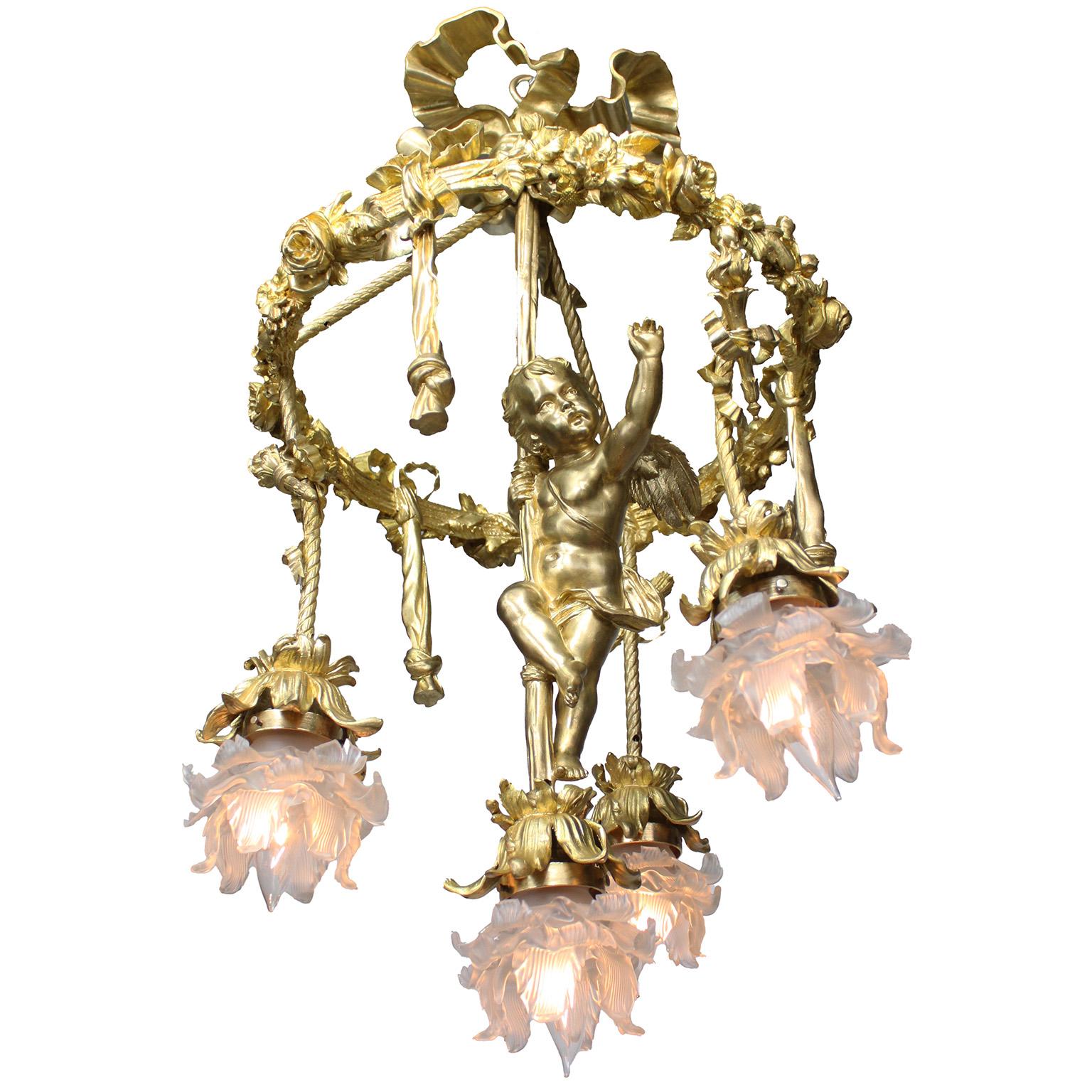 Fino y raro colgante de araña de cuatro luces con forma de querubín o cupido de la Belle Époque francesa en bronce dorado. El ornamentado marco circular de bronce dorado está coronado por flores, cintas y borlas, y tiene tres luces con pantallas de