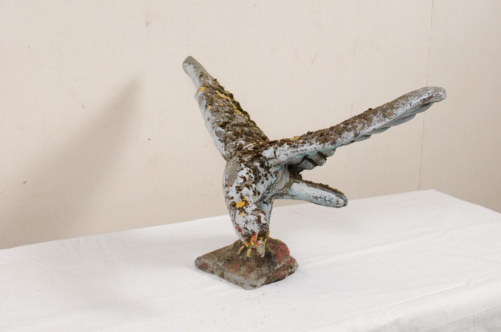 A French bird garden statue in case stone from the mid 20th century. This mid-century statue from France, created in cast-stone, in the image of a bird, standing with head inquisitively down and wings spread upward. This sculptural figure stands