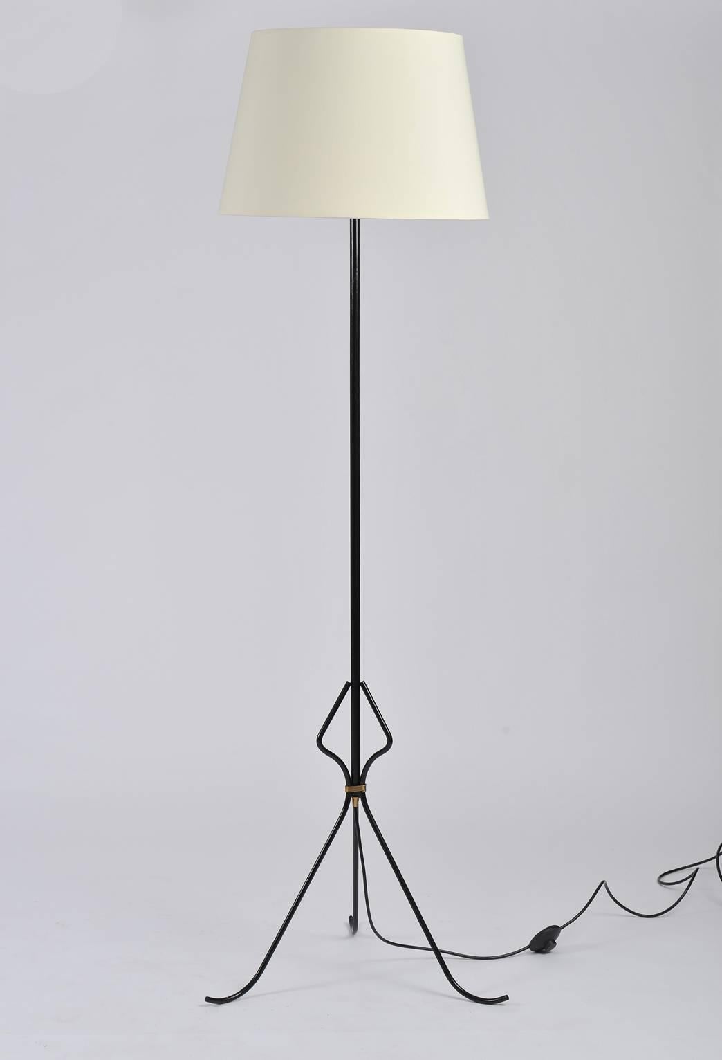 A black enameled iron floor lamp the tripod bass with a brass band detail
with a bespoke ivory fabric tapered shade
France, circa 1950

Dimensions are inclusive of the shade.