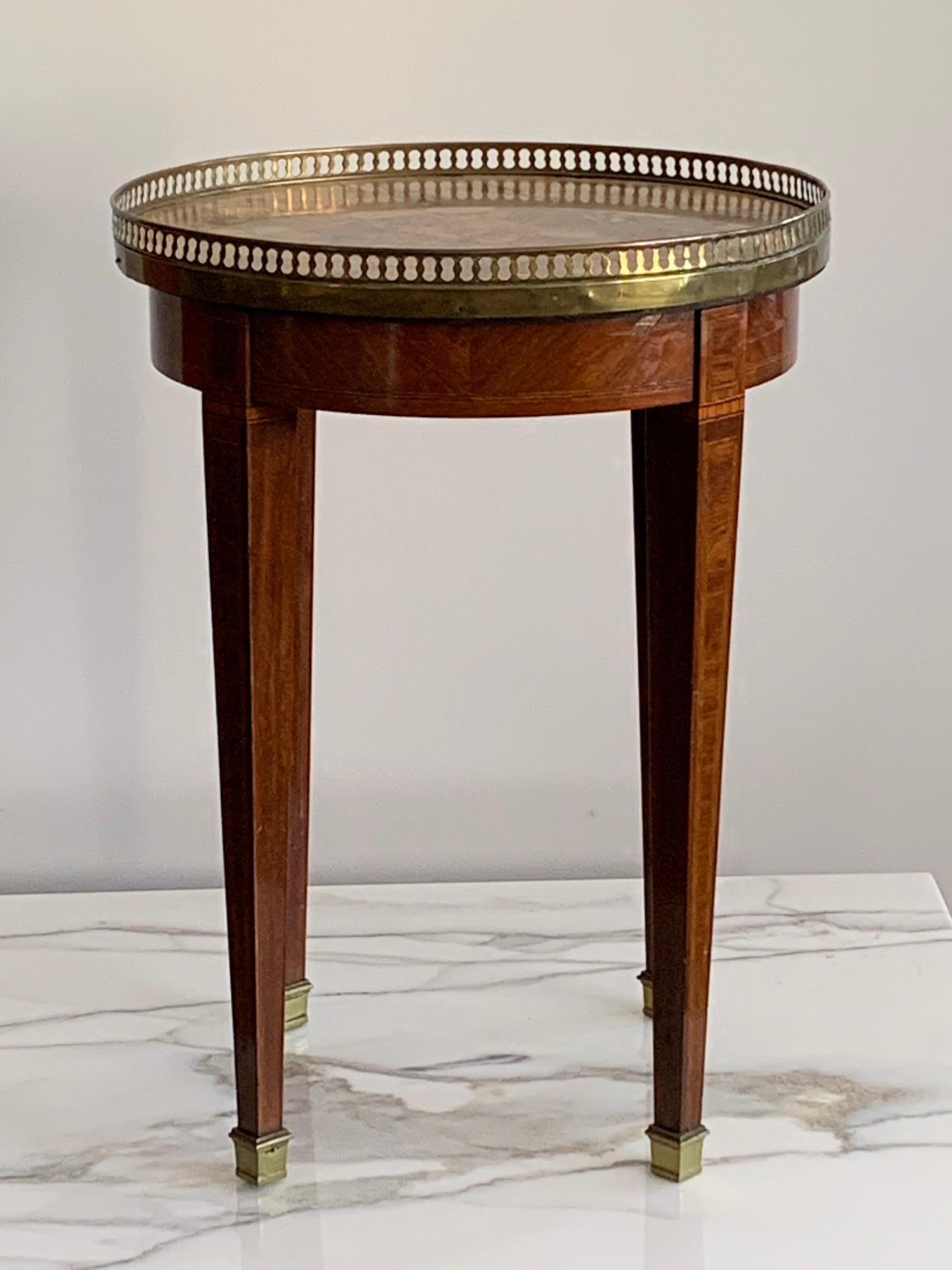 A charming and elegant French bouilotte table with beautiful marble top, brass gallery, tapering legs with inlays and brass sabots. Interesting provenance and history.