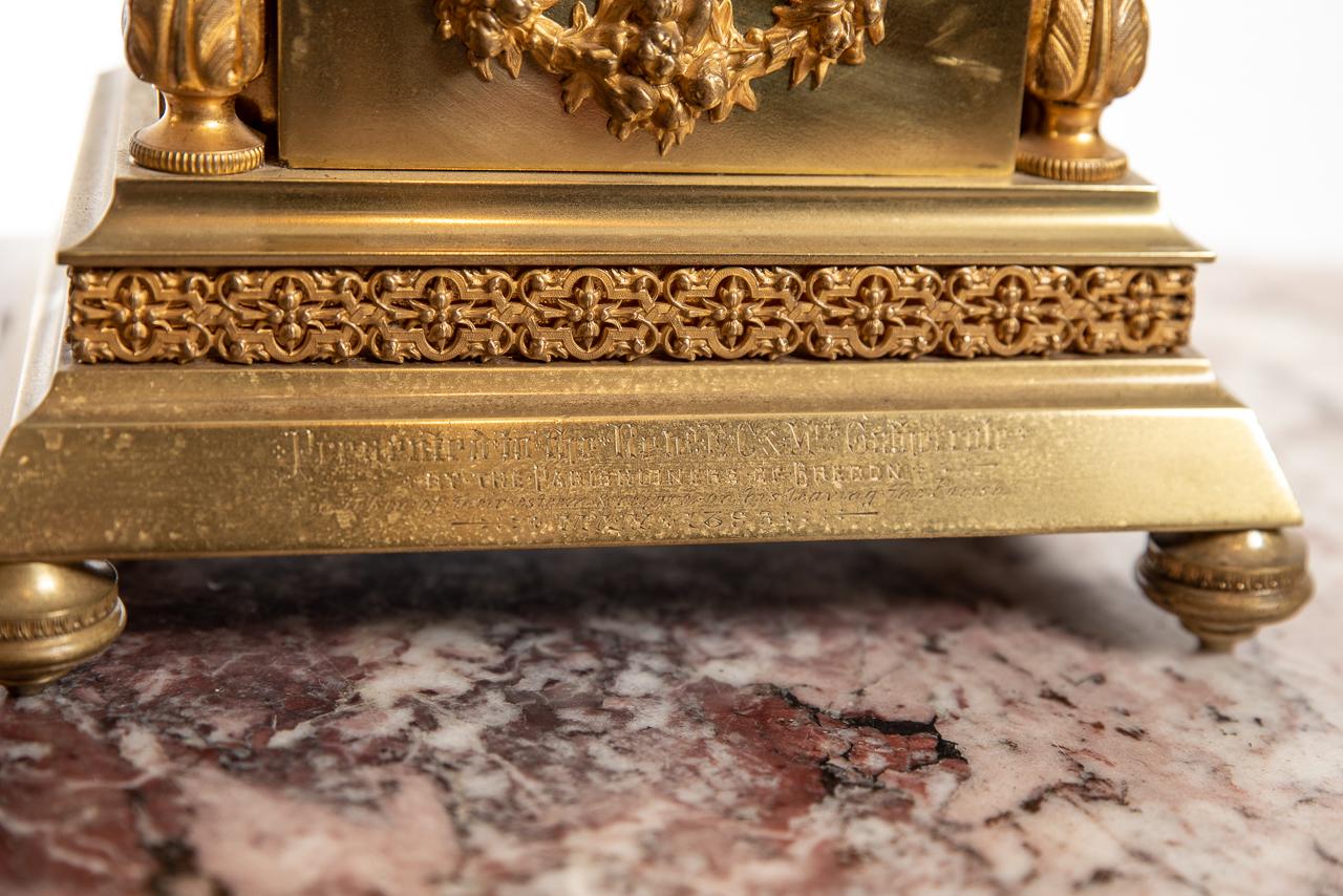 A fine brass case mantel clock with fretwork to the front and sides, with Corinthian columns to the front, along with an Arabic numeral dial and fretwork to the centre. Below the dial being decorated with a brass garland of flowers.
The clock has