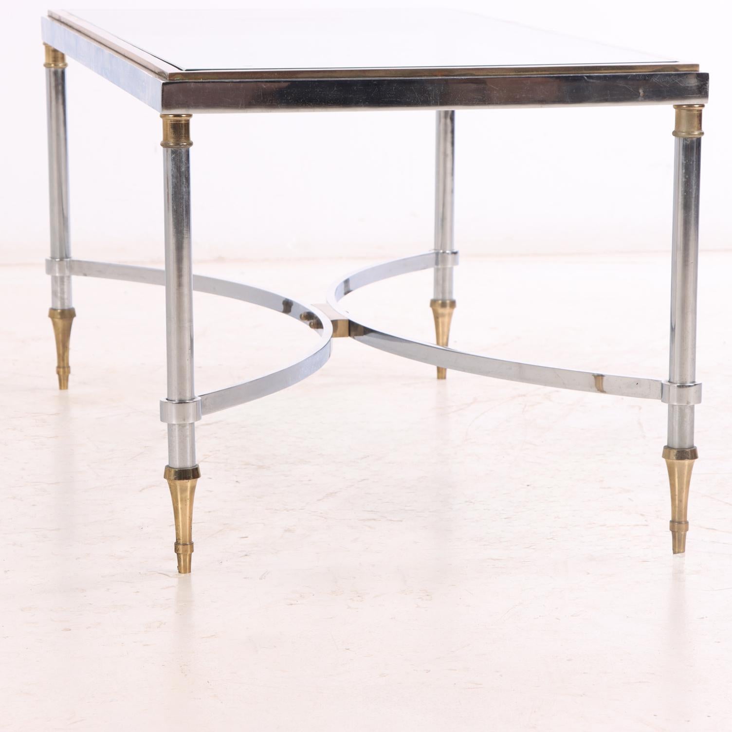 The rectangular glass top rests within a gilt-brass frame, supported by steel legs with brass accents and joined by a stretcher. The design reflects Jansen’s signature neoclassical aesthetic, combining clean modern lines with refined decorative