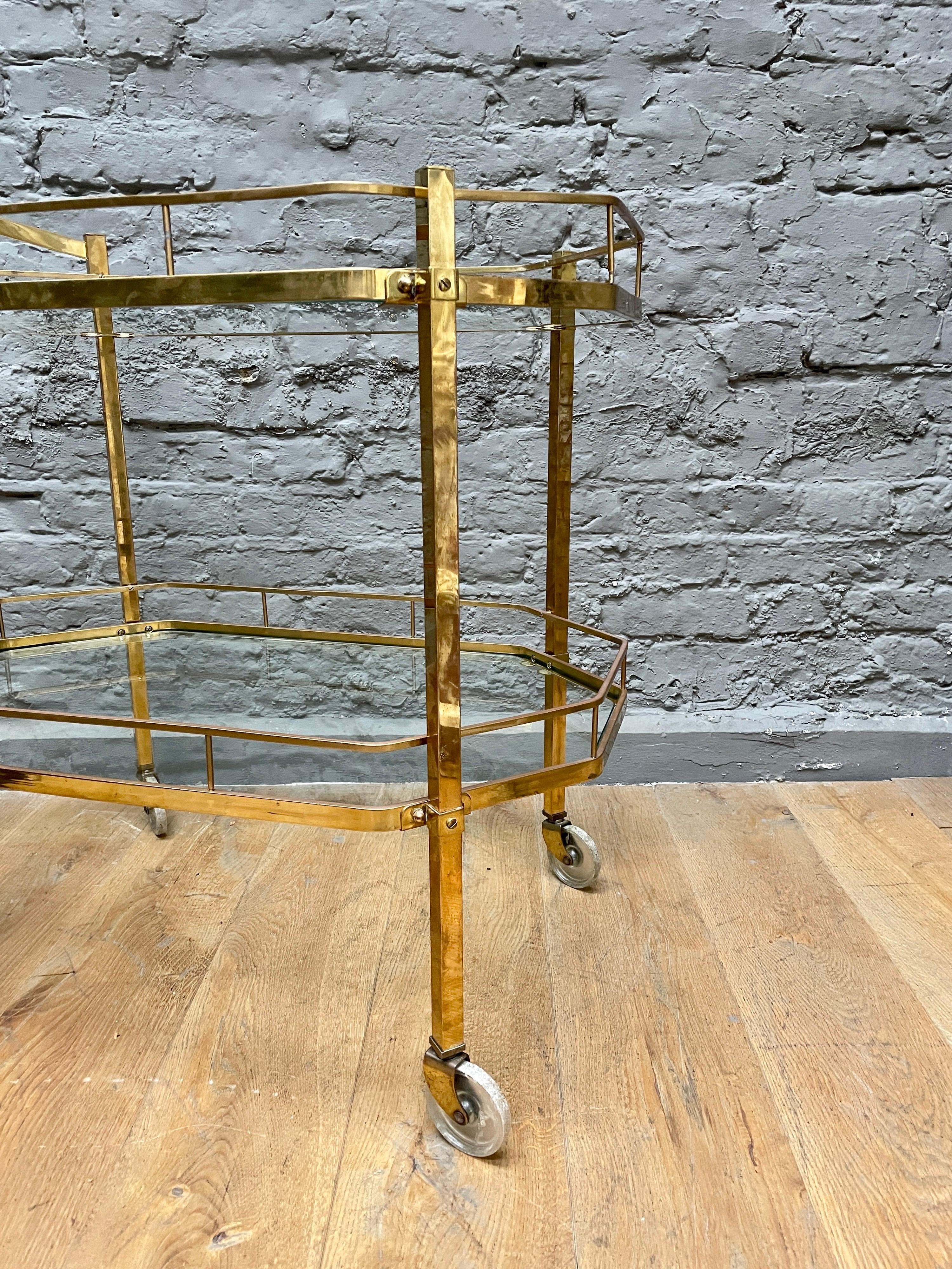 An octagonal shaped two tiered bar cart in brass, with a transferable handle and acrylic wheels. Images are a true reflection of condition, some wear to the lacquer in areas. However an original piece with true patina.