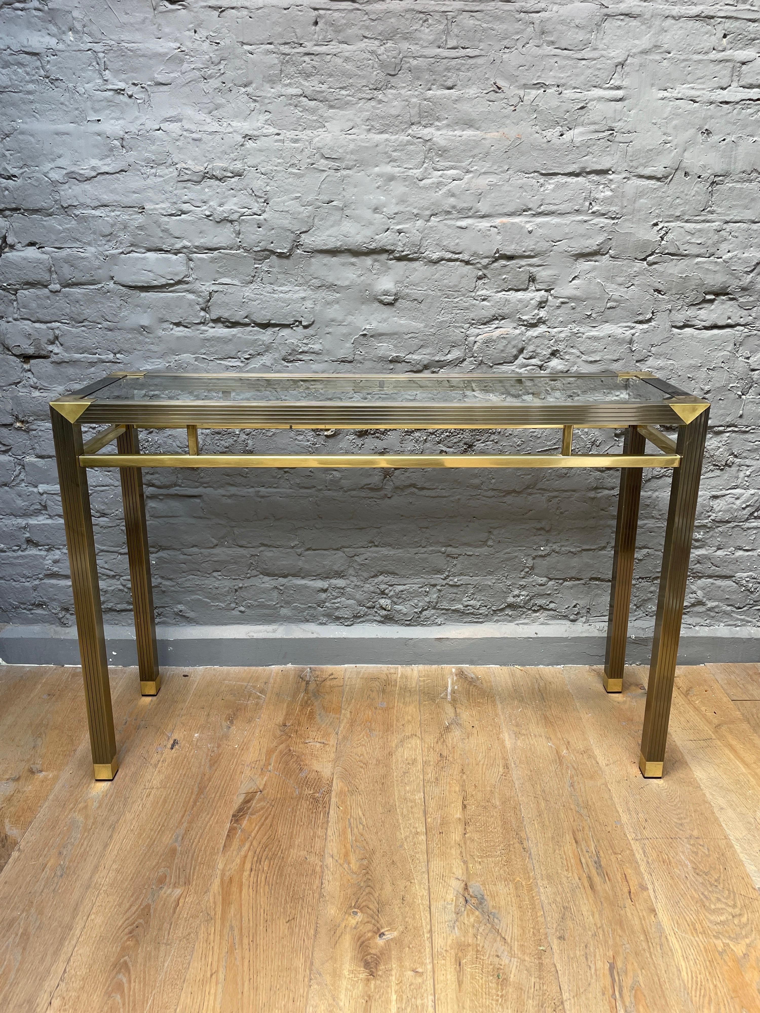 A late 20th century two tone brass console table with glass top. The corners, feet and gallery in polished brass the legs and supports in reeded patinated finish. 

French Circa 1970.