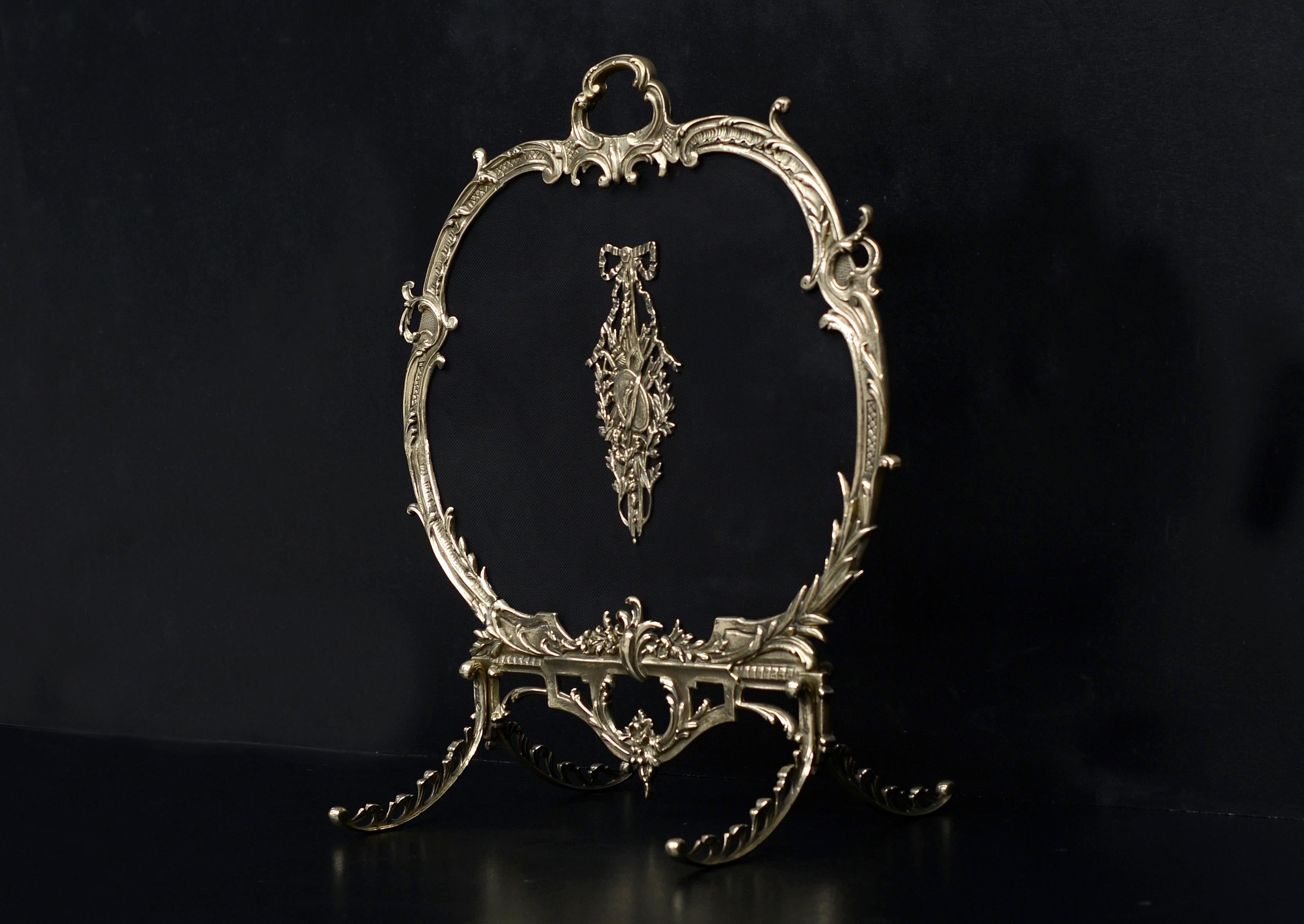 A French brass firescreen with decorative Rococo frame and legs. The fine black mesh behind adorned with brass embellishment with tied ribbon, torch, quiver and shield. 19th century. Unusually small design. (Depth of feet - 14