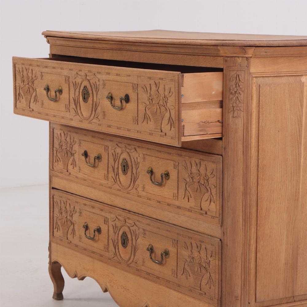 Questo comò presenta dei bei intagli in rilievo che raffigurano due cesti di fiori su ciascuno dei tre cassetti. La finitura è stata rimossa per dare a questo pezzo un aspetto leggero e fresco. La custodia presenta alcuni piccoli segni di usura, ma