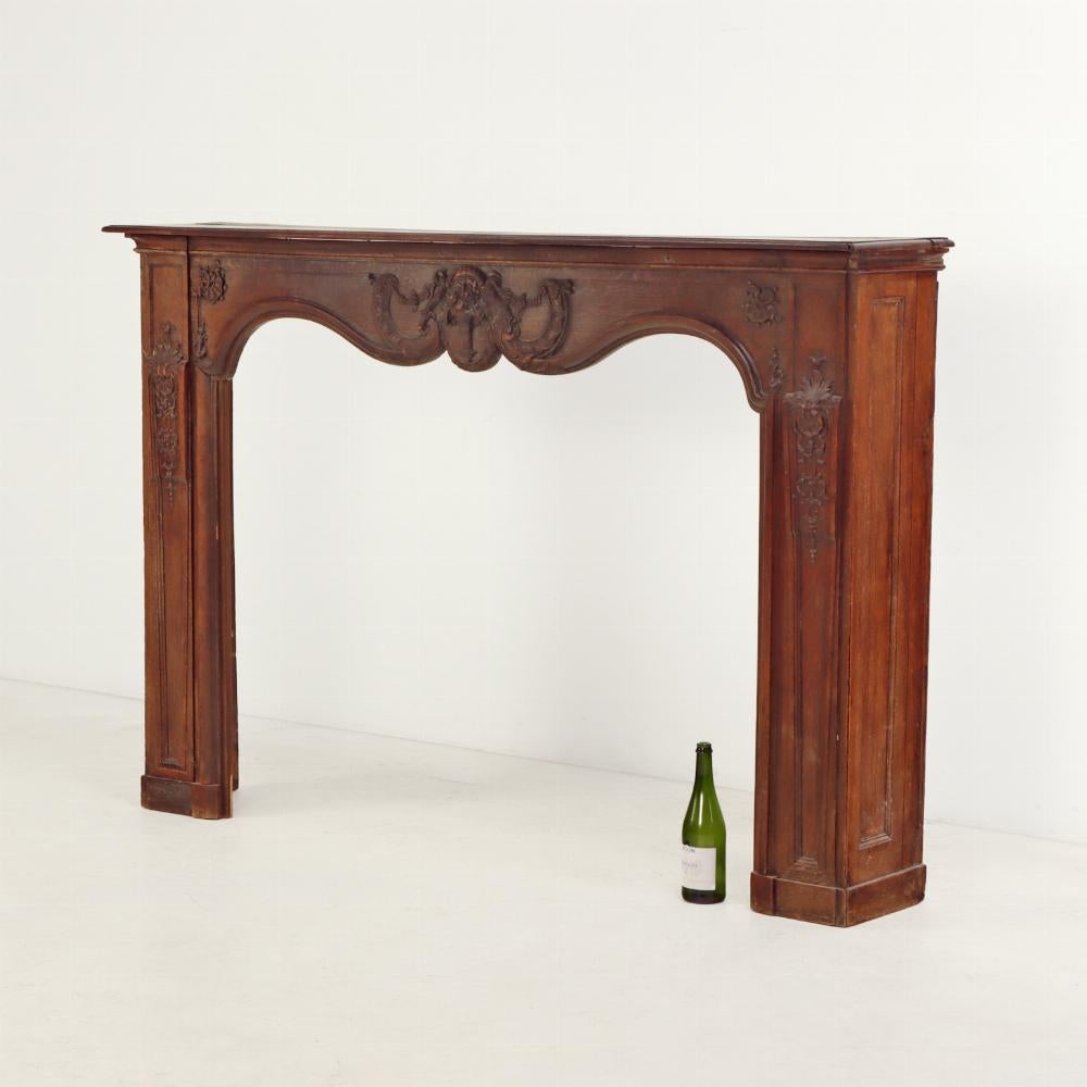 An elegant 18th-century French fireplace mantel, finely carved from solid oak. The shaped apron is adorned with delicate foliate and floral motifs, showcasing the artisanal craftsmanship and decorative sensibility of the period. The soft curves and
