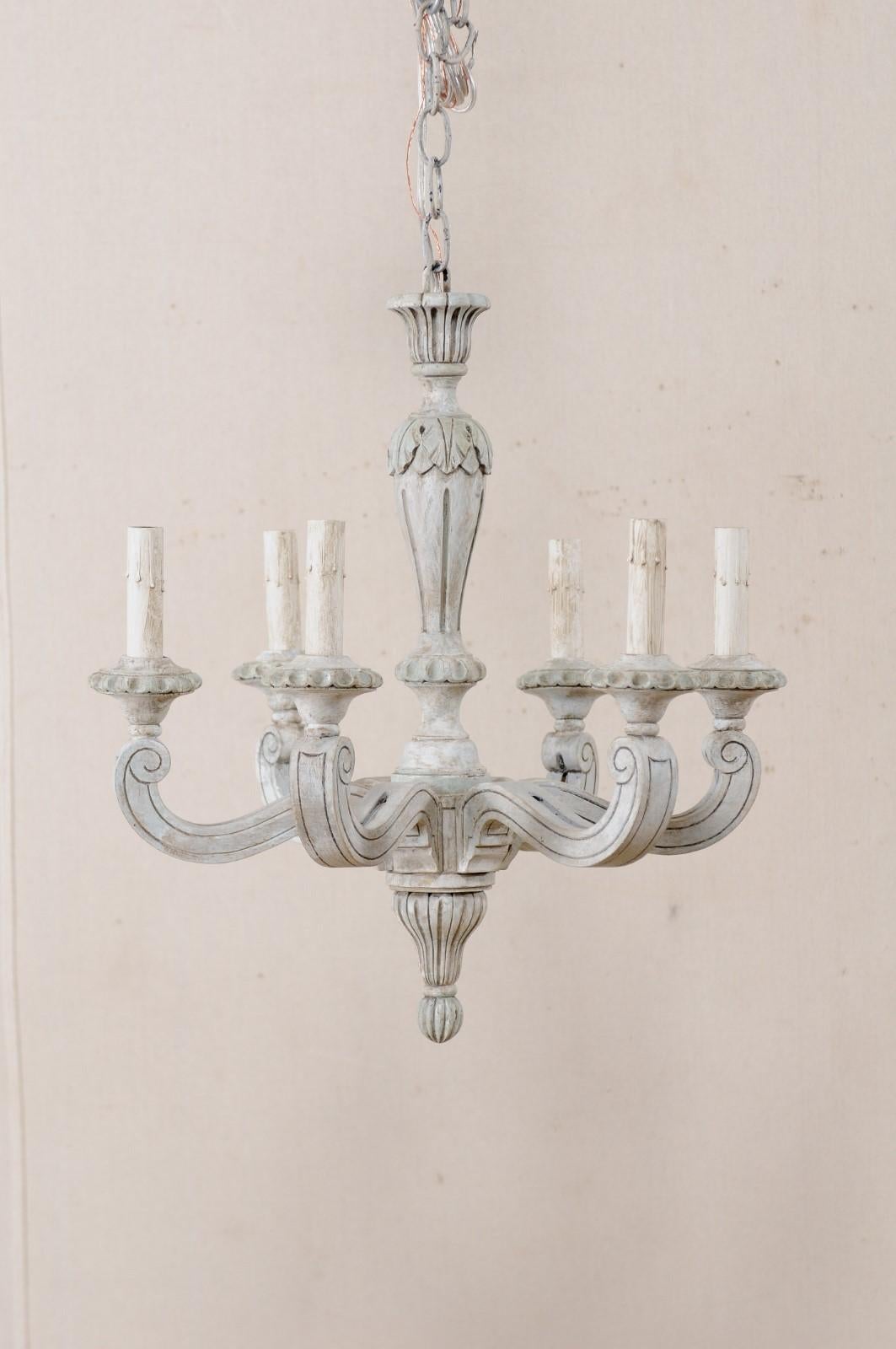 A French mid-20th century carved and painted wood six-light chandelier. This lovely mid-20th century chandelier from France features a carved central column carved with fluted accents and a leaf motif six wooden arms emerge outward and up from the