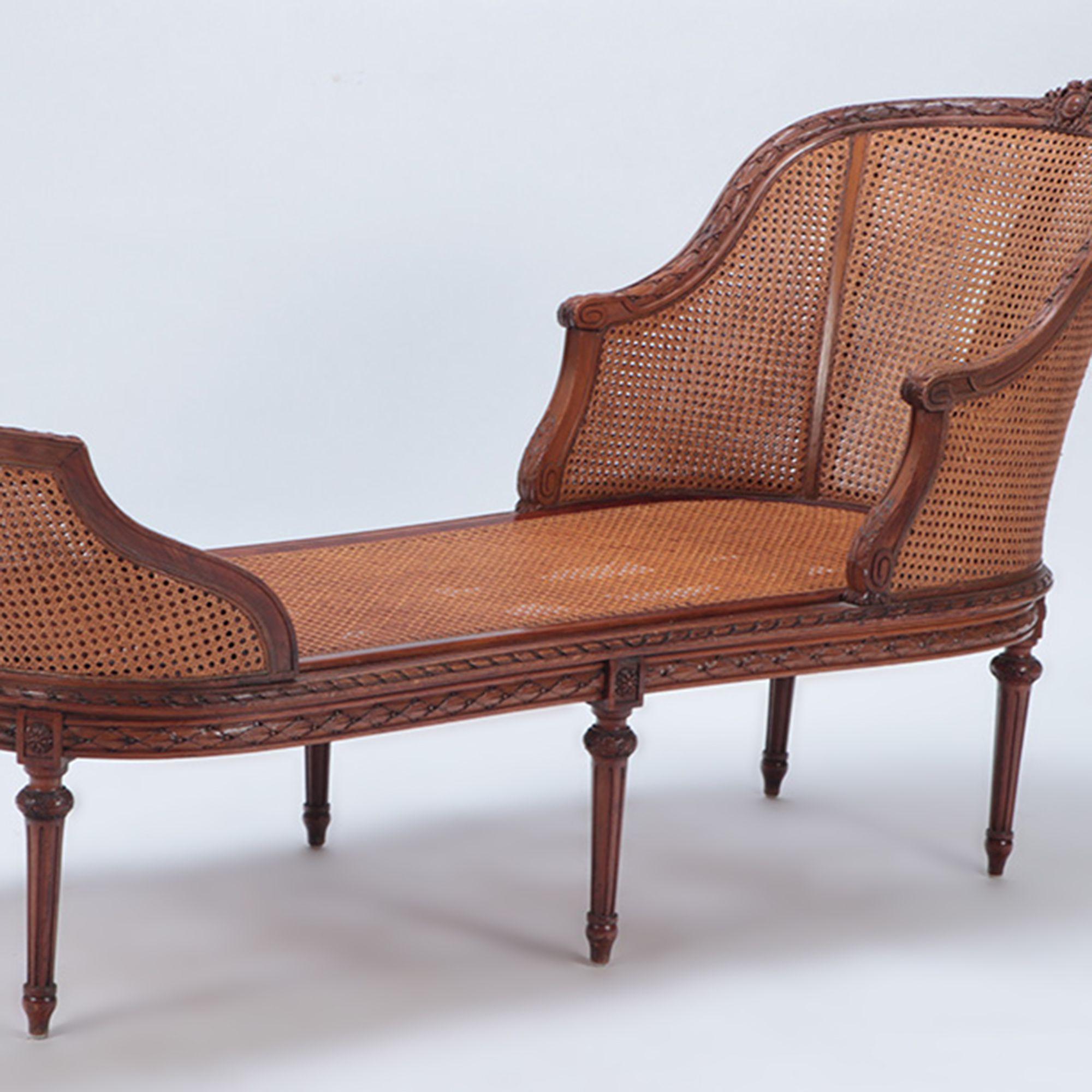A French carved walnut chaise lounge in the Louis XVI style having double cane and loose cushion upholstery and resting on six fluted and round tapered legs.Rosettes along the bottom rail at each knee, circa 1900.