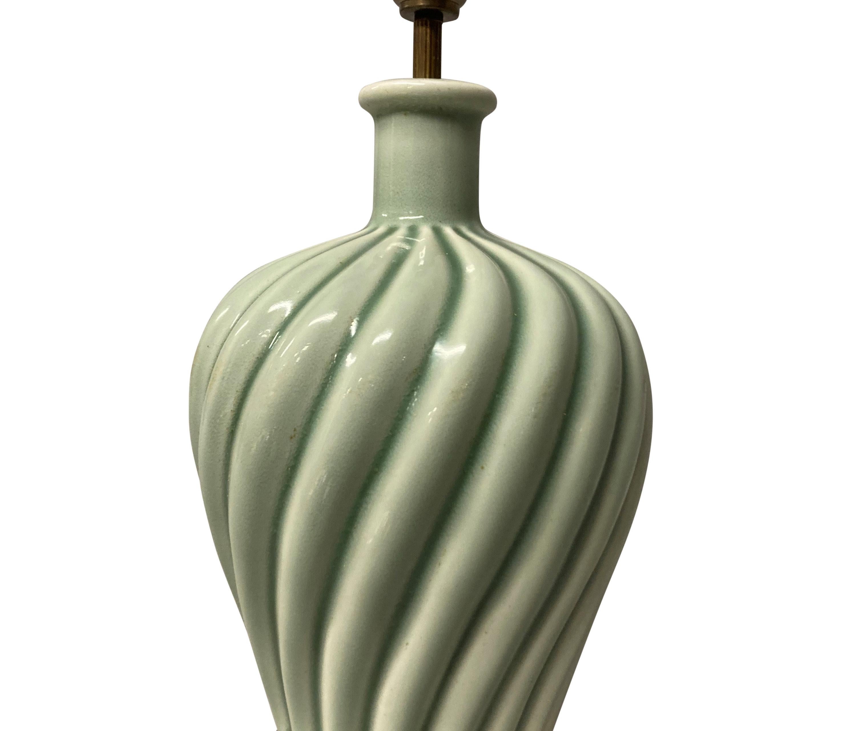 A French celadon glazed ceramic lamp of a swirl design, mounted on an ebonised plinth base.