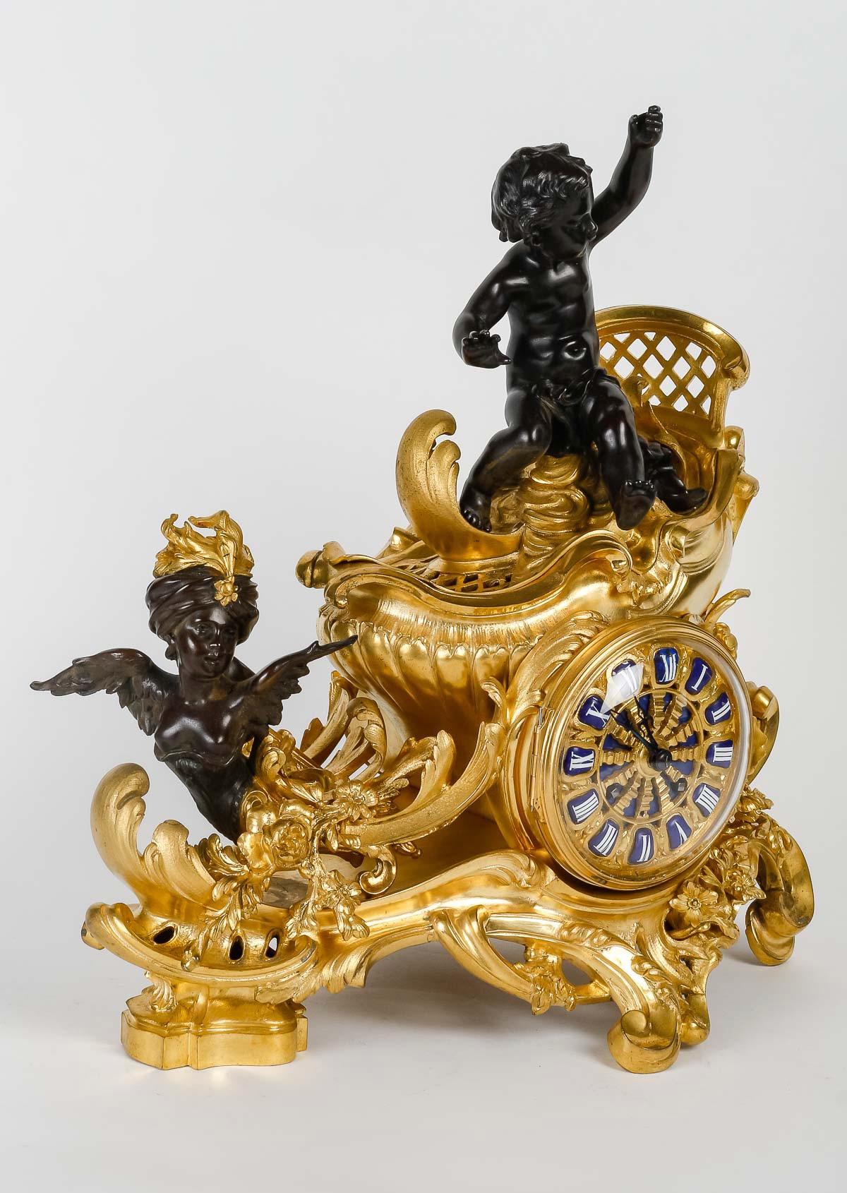 A French Ormolu and Patinated-Bronze ‘Chariot’ Three-pieces Clock Garniture
Attributed to François Linke (1855 - 1946), Paris, Late 19th/ Century 

The clock representing a putto on a chariot pulled by a winged female bust with turban, on