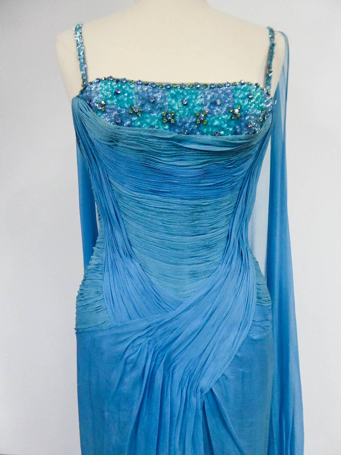 Circa 1960/1970
France
Haute Couture evening dress from Carven House Designer in blue silk muslin from the 60s/70s. Bustier with thin straps and large low-cut neckline embroidered with blue and green sequins in roses and cabochons set with glass