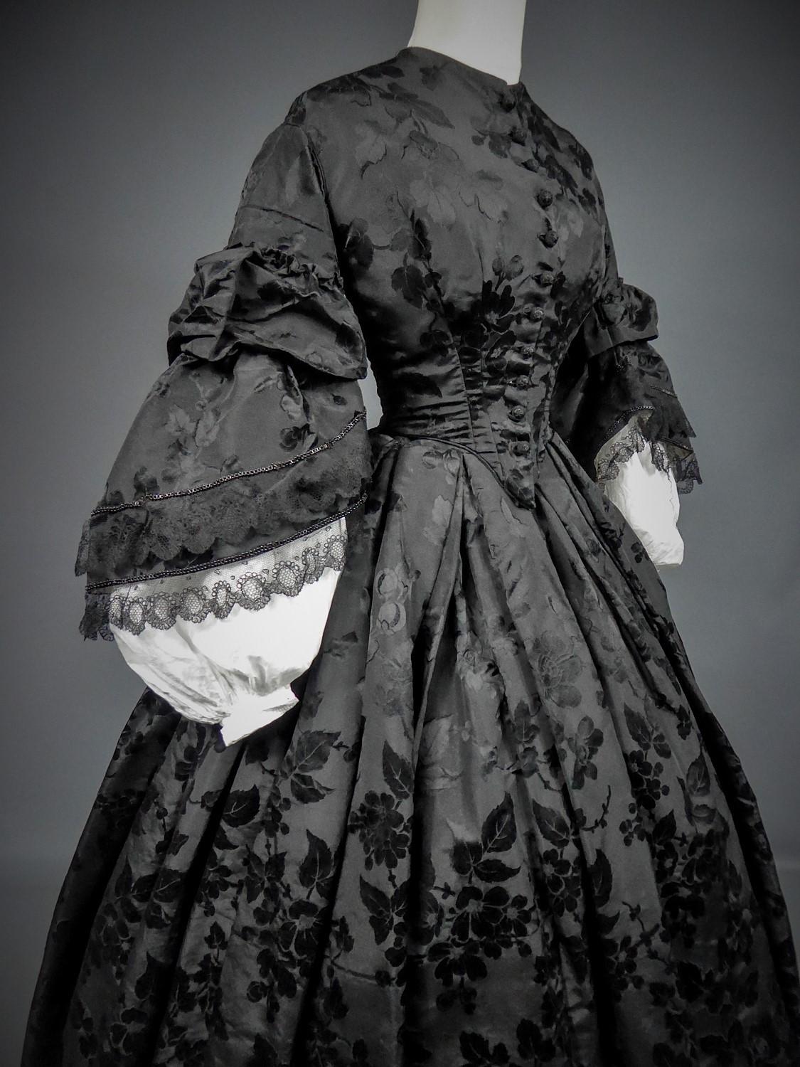 Circa 1862/1865
France

Mourning crinoline dress (bodice and skirt) in flowery damask silk faille dating from the end of the Second French Empire. Bodice and adjoining skirt in satin damask faille or Gros de Tour. Lined and boned bodice with large