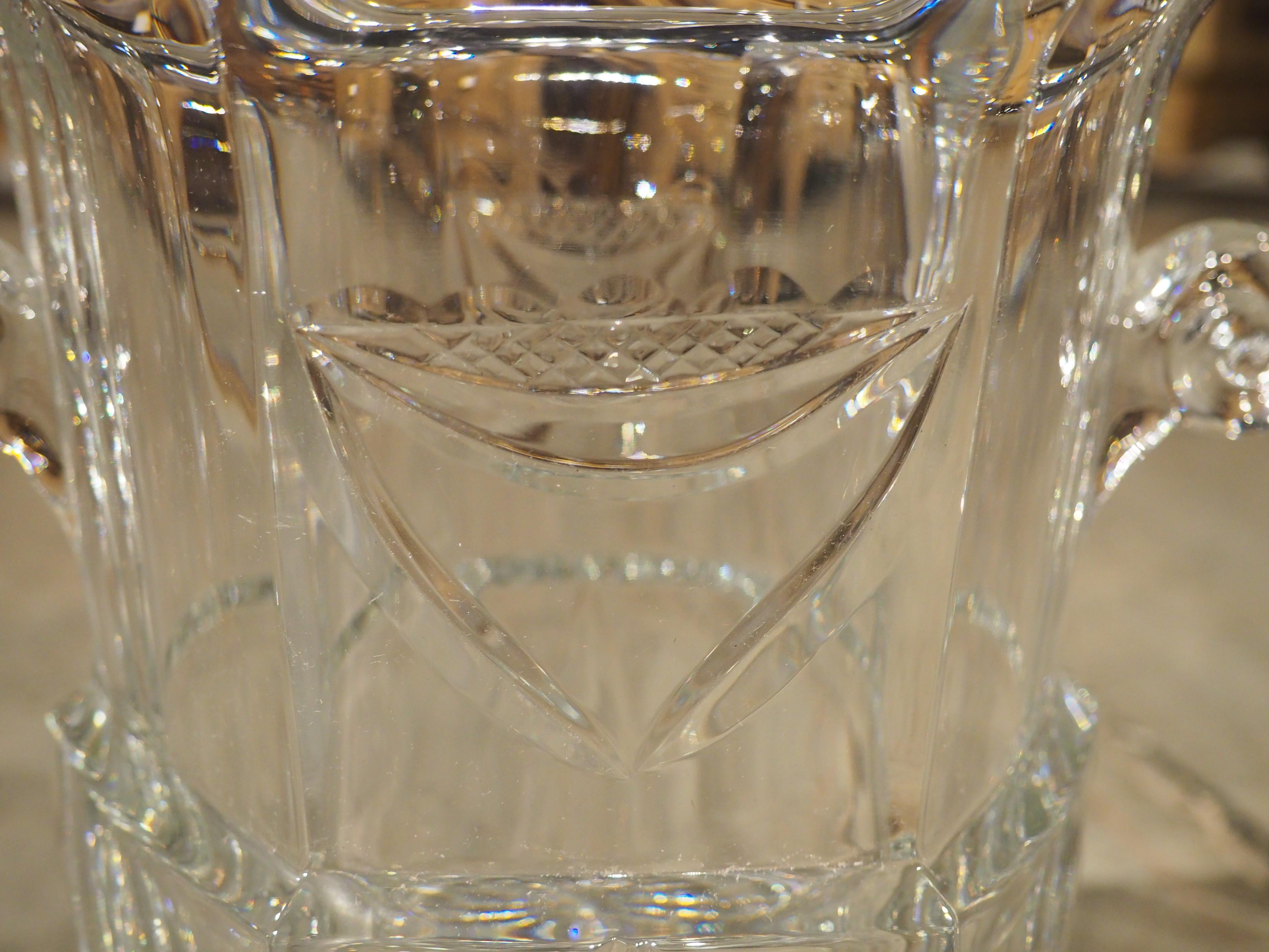 Hand-blown in France during the 1900s, this beautiful crystal champagne bucket has exquisite detailing of a pair of escutcheons, each aligned above a tripartite leaf. A pair of two small volute handles are situated high up on the hexagonal body,