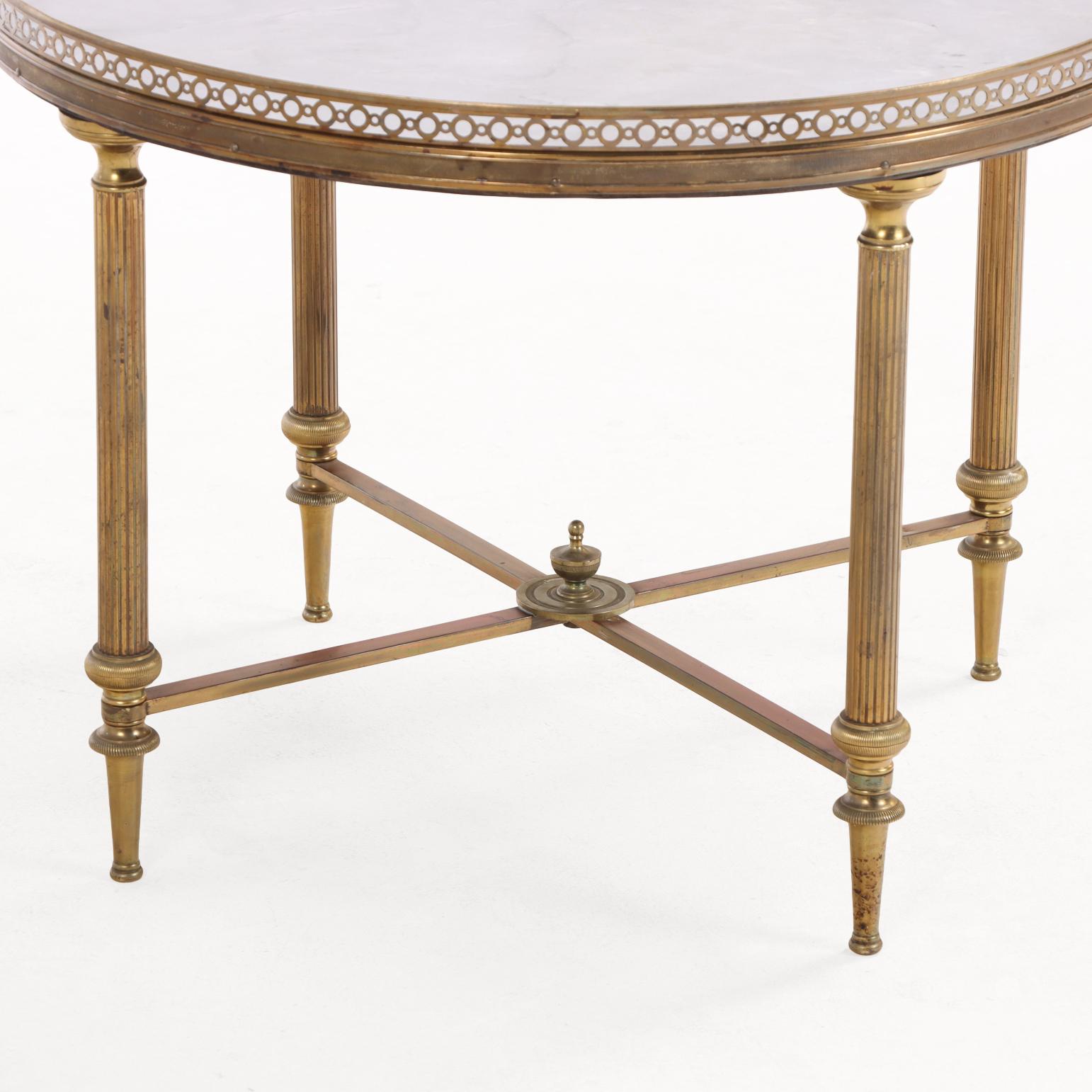 This elegant table features a marble top inset into a pierced brass gallery, supported by a four-leg base joined by a cross stretcher and surmounted with a decorative finial. Exemplifying Directoire-inspired design, it combines refined detailing