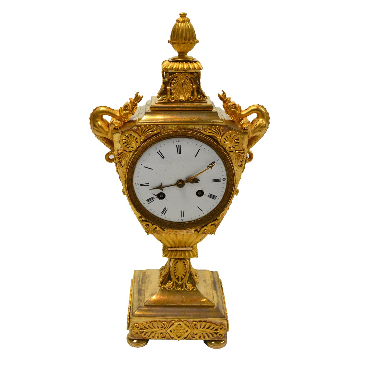 An rare model French Empire mantle clock featuring a classical urn with dragon handles. The clock is entirely of gilded bronze with original fire gilding. The urn-shaped case is surmounted with a pineapple finial; on either side of the 4.5? White