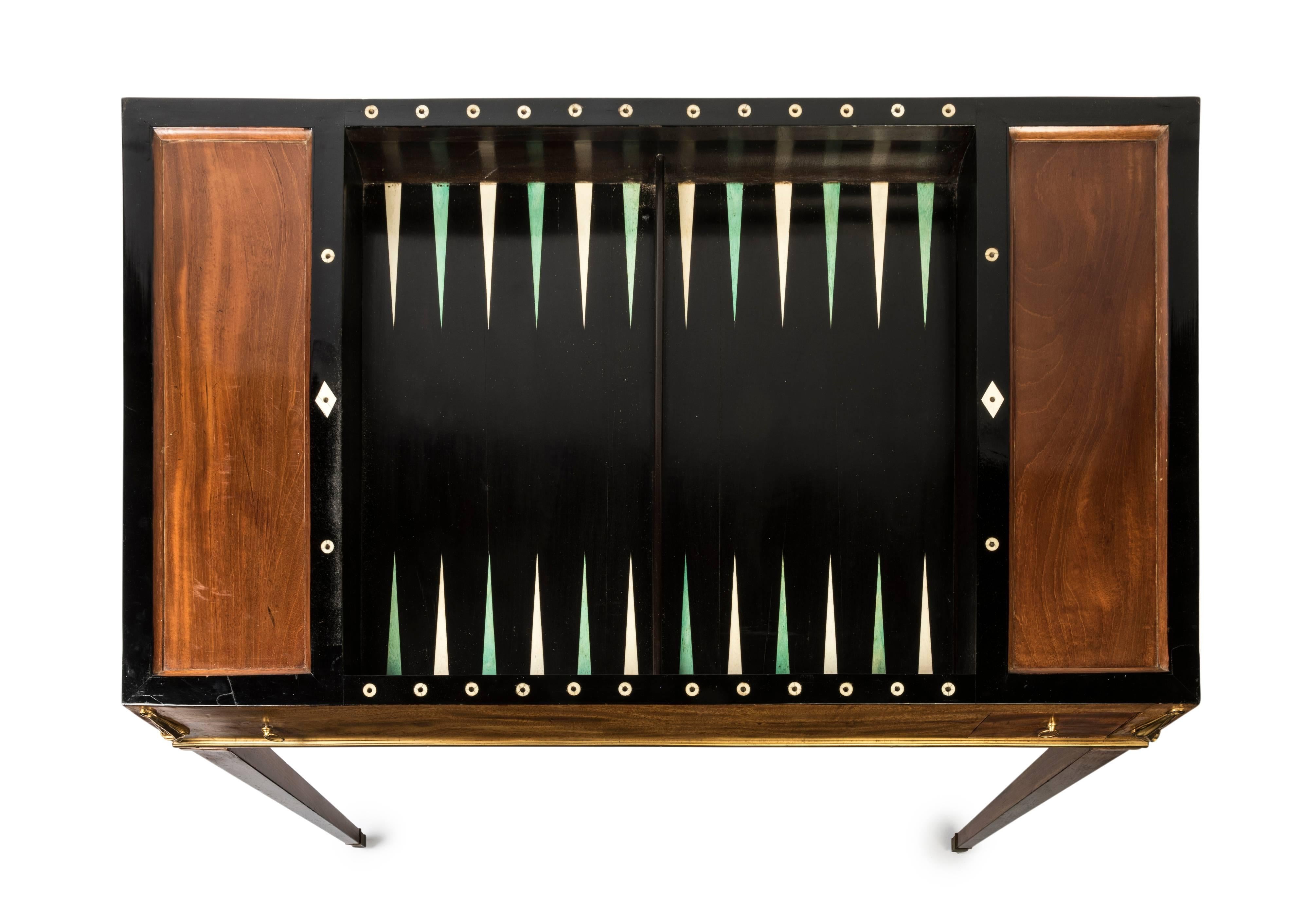 A French early 19th century Georgian games table,
the removable tooled leather inlaid top revealing internal backgamon board in ebonised frame, flanked by recessed panels, the frieze with two ring handles, with single games drawer, the other