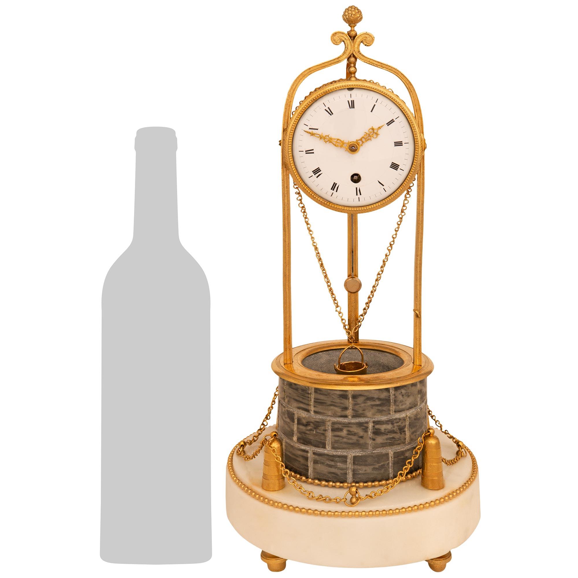 Un affascinante e unico orologio francese dell'inizio del XIX secolo in stile Luigi XVI. Ormolu, marmo bianco di Carrara e marmo grigio di Sant'Anna. Questo adorabile orologio a forma di pozzo poggia su una base circolare in marmo bianco di Carrara