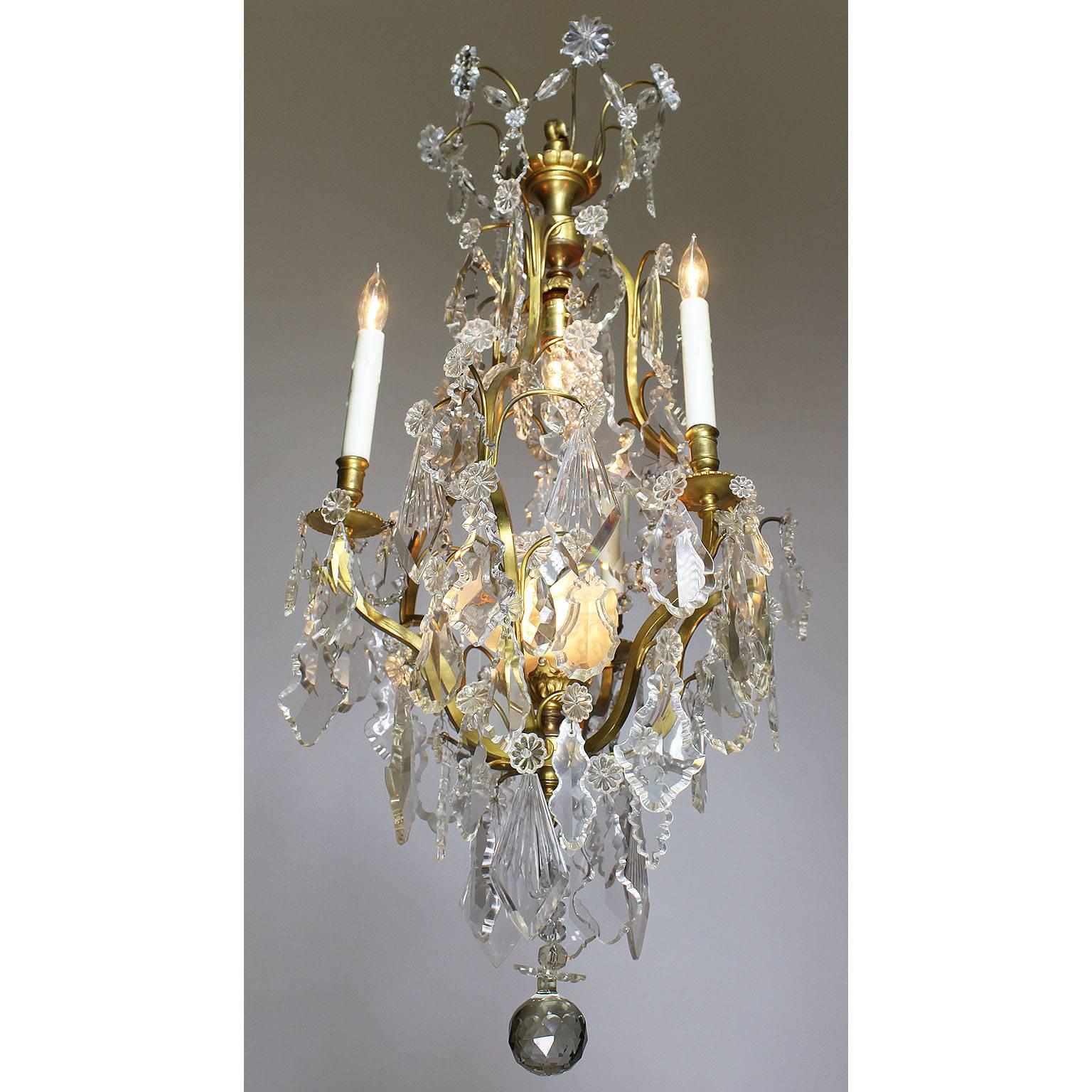 A French early 20th century Louis XV style gilt bronze and cut-glass three-light chandelier. The elongated gilt-metal body with cut-glass pendants, surmounted with three scrolled candle amrs and two interior lights, the lower one with a floral