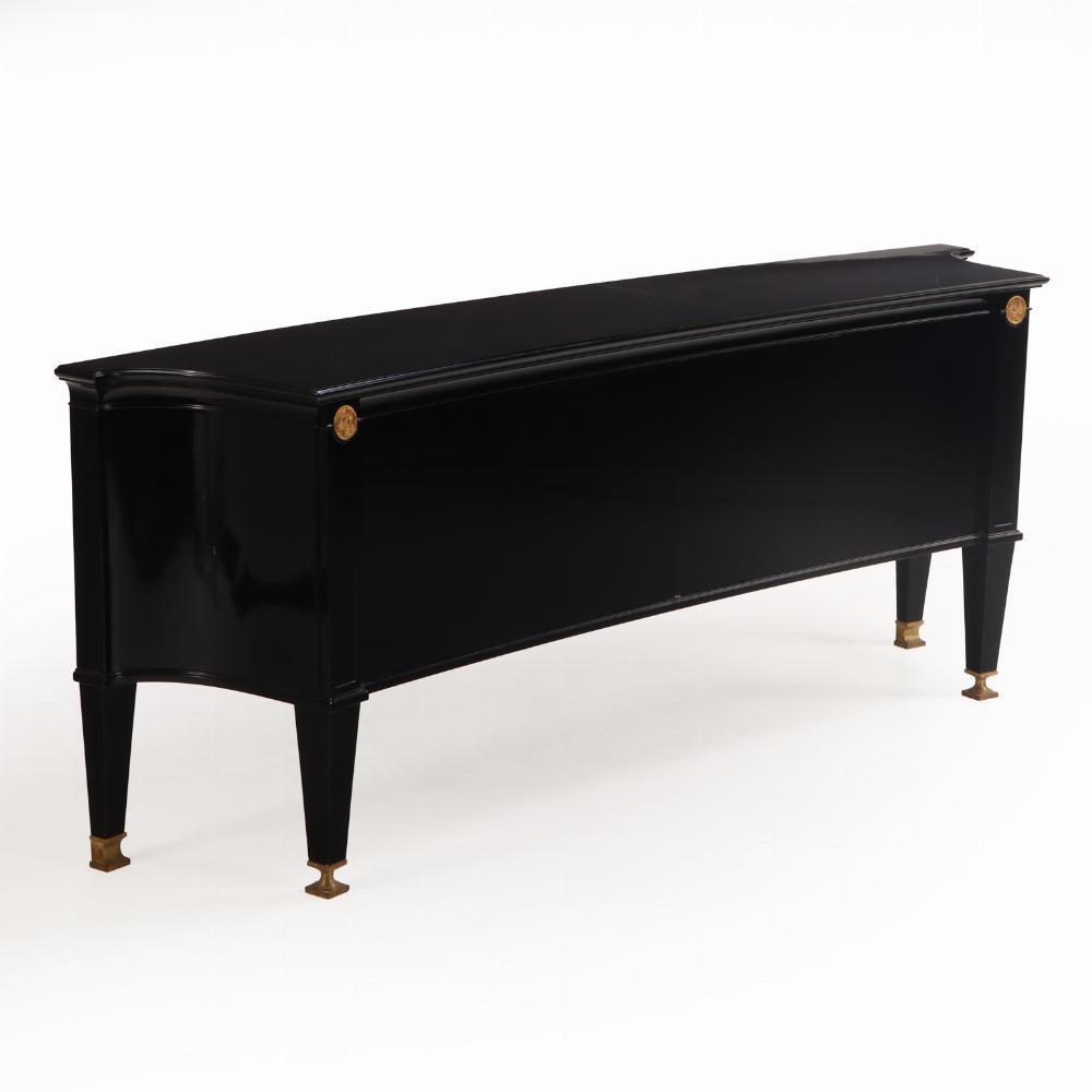 Un escultural aparador francés, de hacia 1940, realizado en madera ebonizada con elegantes monturas de bronce, en el refinado estilo neoclásico asociado a André Arbus. El frontal sutilmente curvado y los laterales más dramáticamente curvados añaden