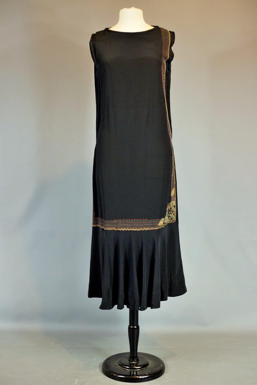 Um 1930/1935
Frankreich oder Europa

Weites Kleid aus schwarzem ottomanischem Seidenkrepp, bestickt mit polychromem Zickzack im ägyptomanischen Stil der 1930er Jahre. Schräg genähtes, ärmelloses, gerades Kleid mit mechanischer Stickerei, die von der
