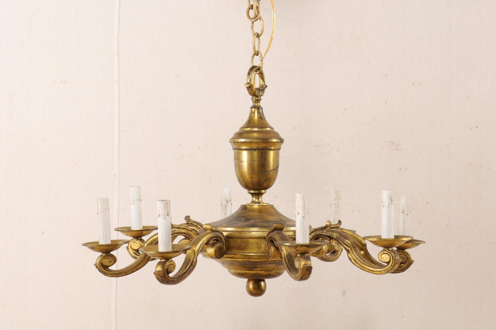 A French gold toned metal eight-light chandelier from the mid-20th century. This vintage chandelier from France features an overall round-shape, with curvy central column, whose more bulbous section supports the light arms. Eight s-style arms extend
