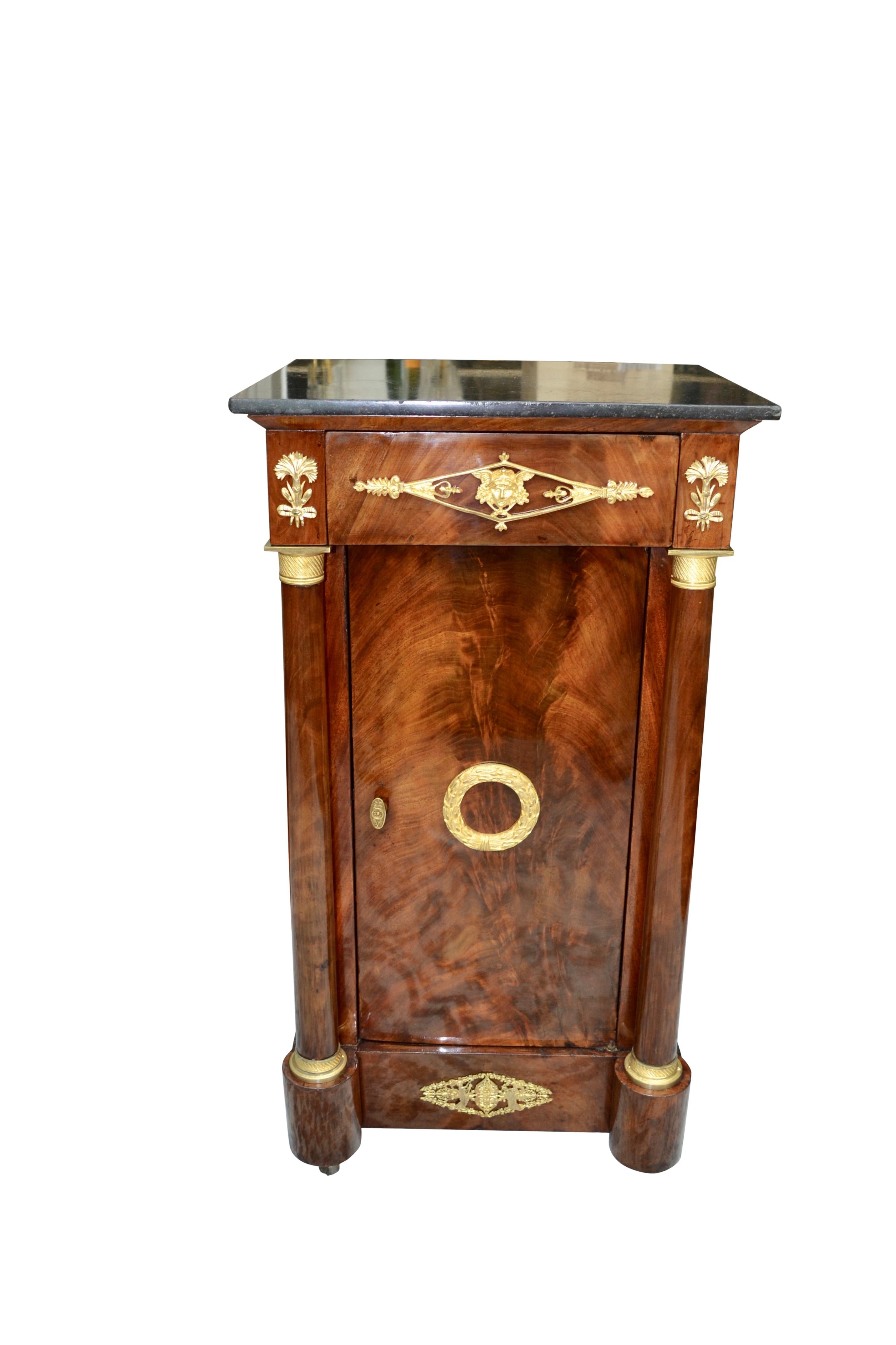 A beautifully veined mahogany bedside table (referred to as a Somno), which was a popular piece of furniture during the French Empire period. There is a single top drawer below a fixed grey black marble top, which is flanked by two turned mahogany