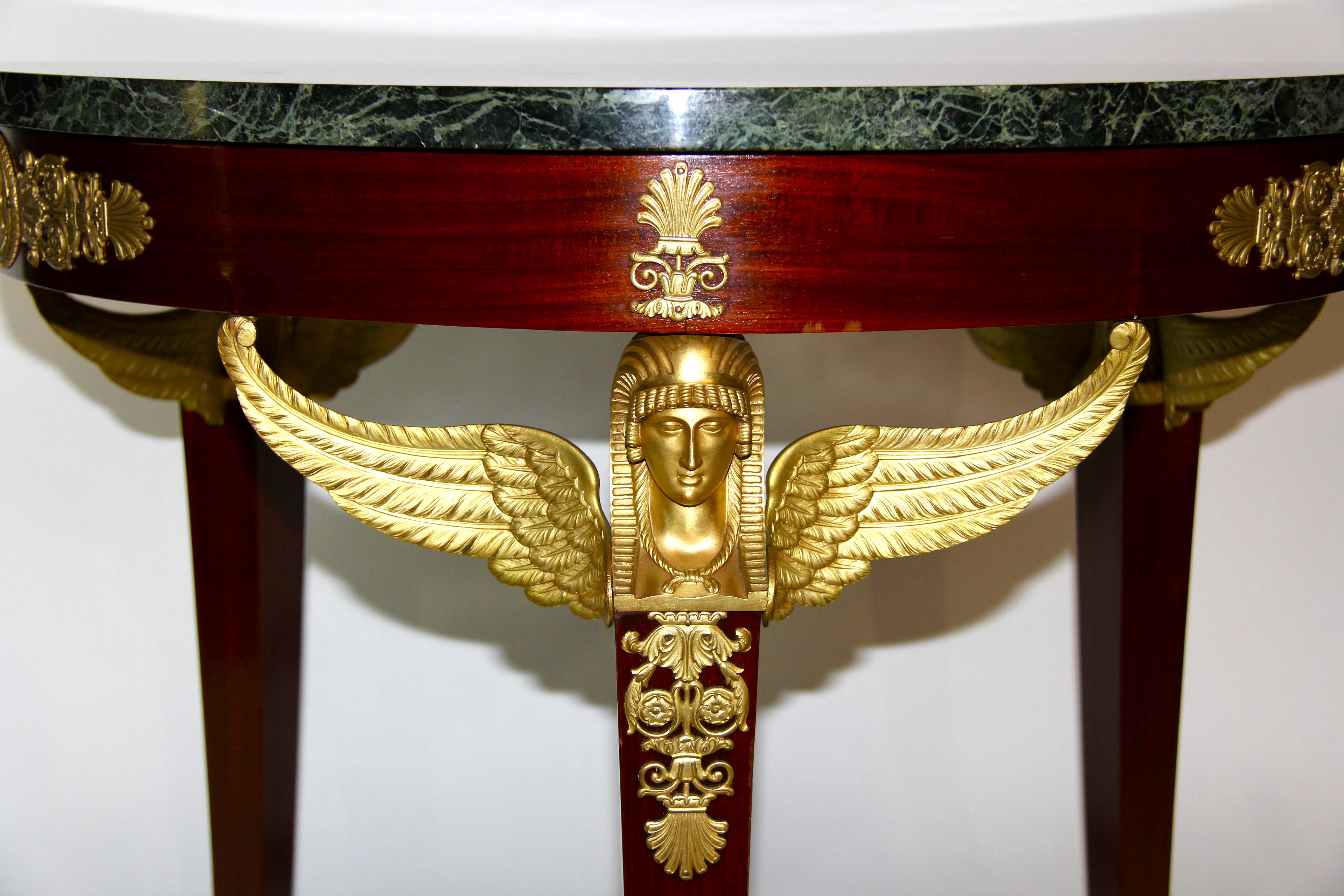 Mesa de centro/guéridon del Imperio francés con monturas figuradas aladas de bronce del Renacimiento egipcio, con encimera circular de mármol Verde Antico, apoyada en una base de caoba con monturas de bronce dorado. La encimera de mármol es de color