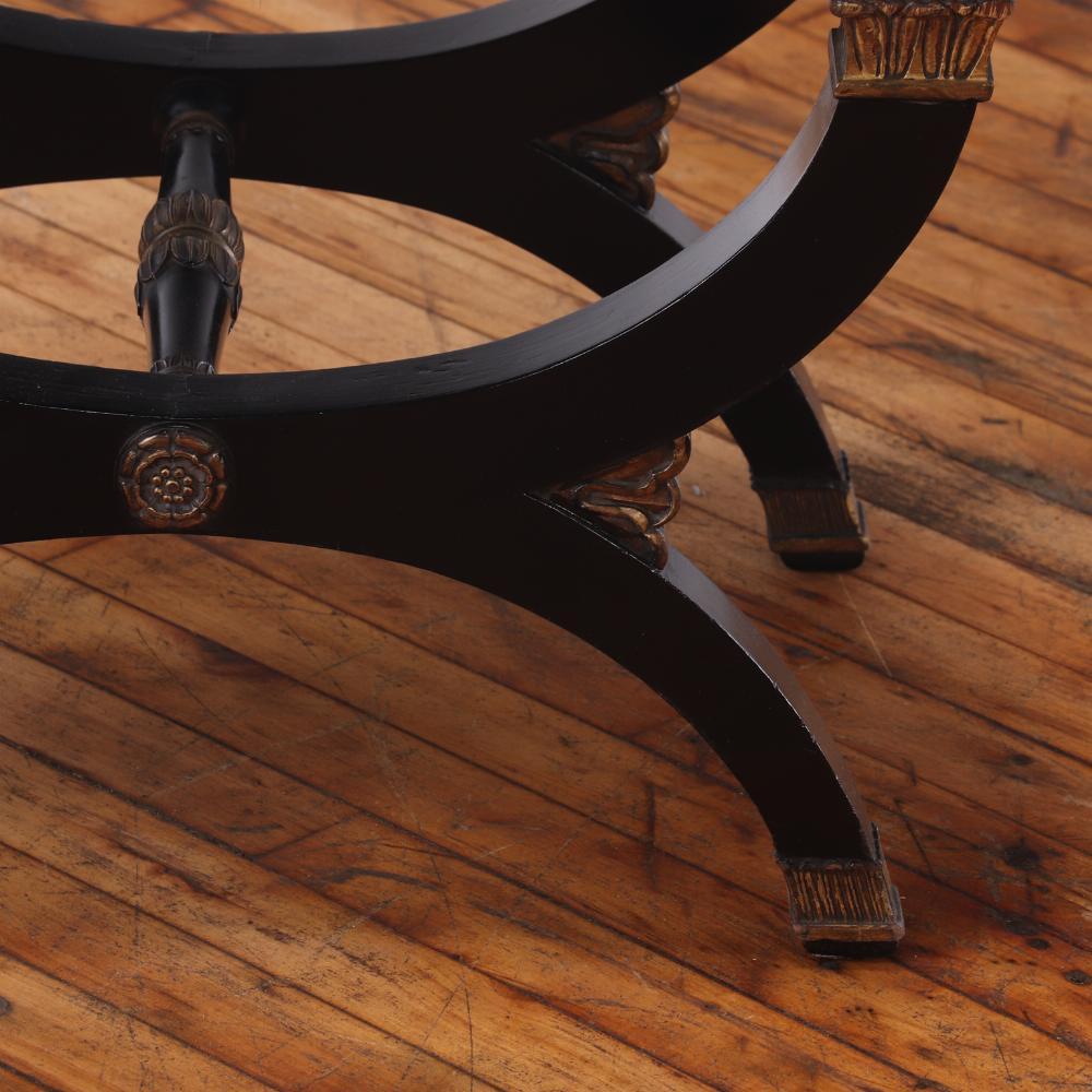 This X-frame stool has a deep ebonized frame with lovely giltwood embellishments. The X-shaped supports are joined by a central stretcher and surmounted by a neutral upholstered seat. Perfect in front of a vanity or as a piano stool.