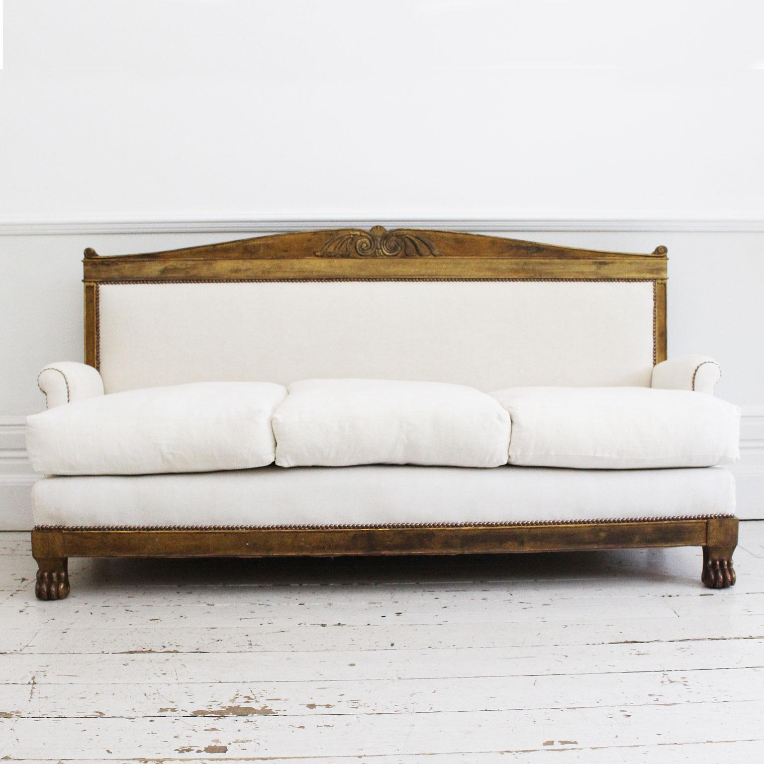 This grand gold gilt antique French sofa is in the Empire style, dating from the late 19th century. It has been newly upholstered in antique French linen, feather filled cushions and finished throughout with studs. We love claw feet detail.