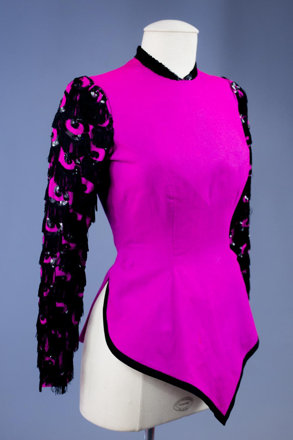 Vers 1938/1942
France
Étonnant boléro du soir, peut-être Haute Couture Worth (transmission orale de la descendance), en sergé de laine fuschia Circa 1938/1942. Boléro courbé avec fourreau marquant les hanches, avec coupe diagonale en losanges. Col