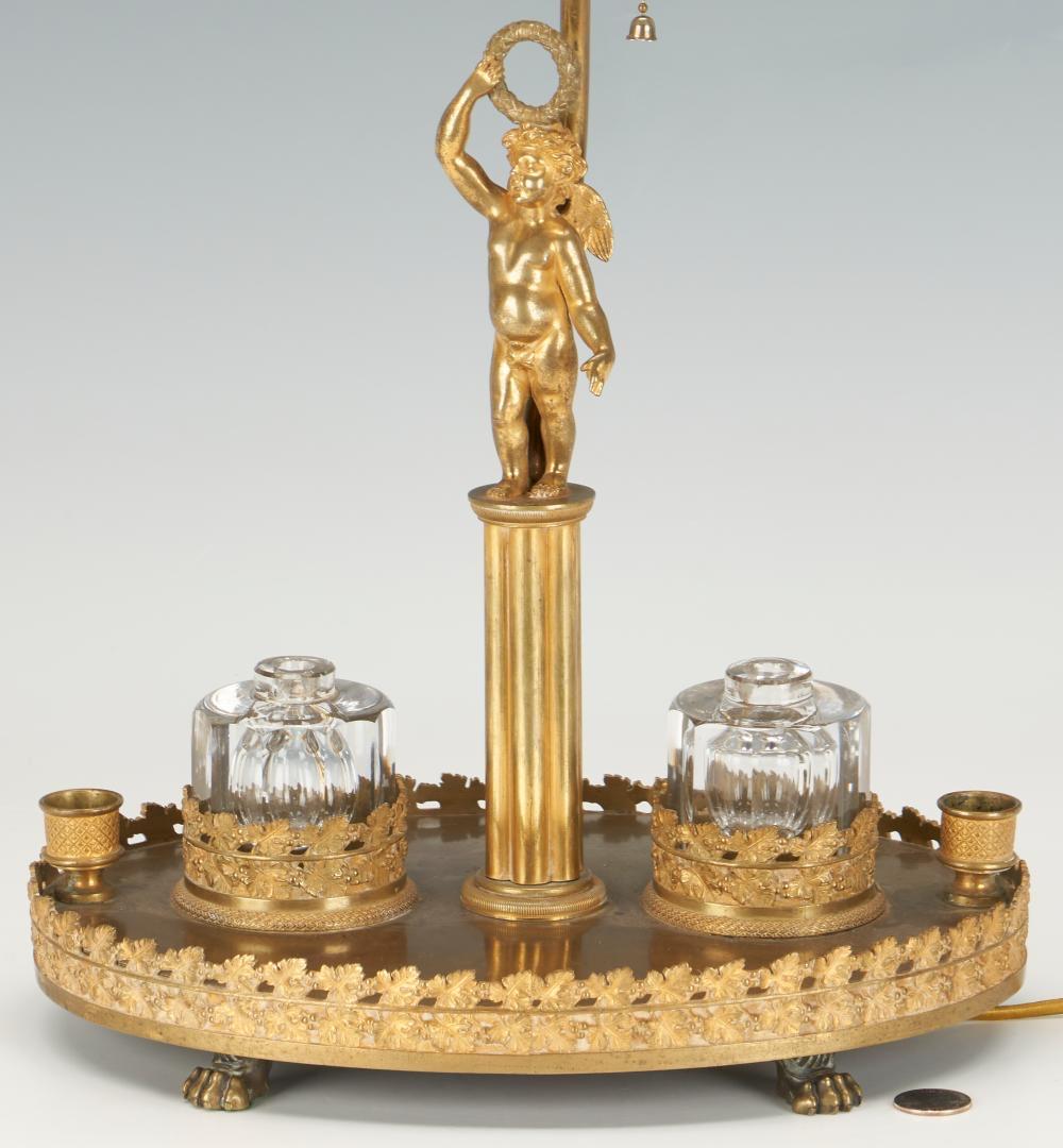 A French Figural Bronze Inkwell Desk Lamp with Tole Shade, Late 19th / Early 20th Century

French double inkwell figural bronze desk lamp, comprised of a central winged bronze cherub figure holding a laurel wreath above his head flanked by two glass