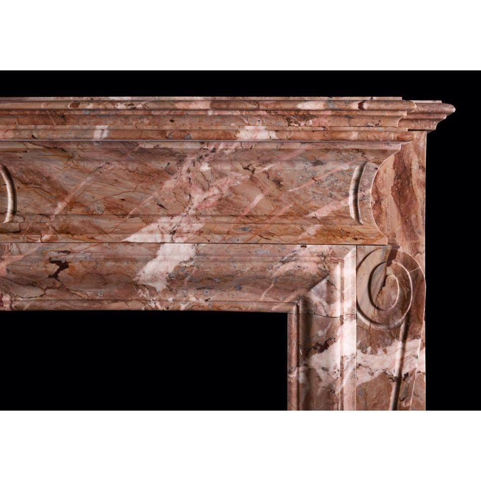 Cheminée française du XIXe siècle en marbre Sarrancolin. Les jambages moulurés avec des volutes au sommet sont surmontés d'une frise incurvée avec une coquille sculptée au centre. Etagère moulurée au-dessus. Les bouches d'aération en laiton