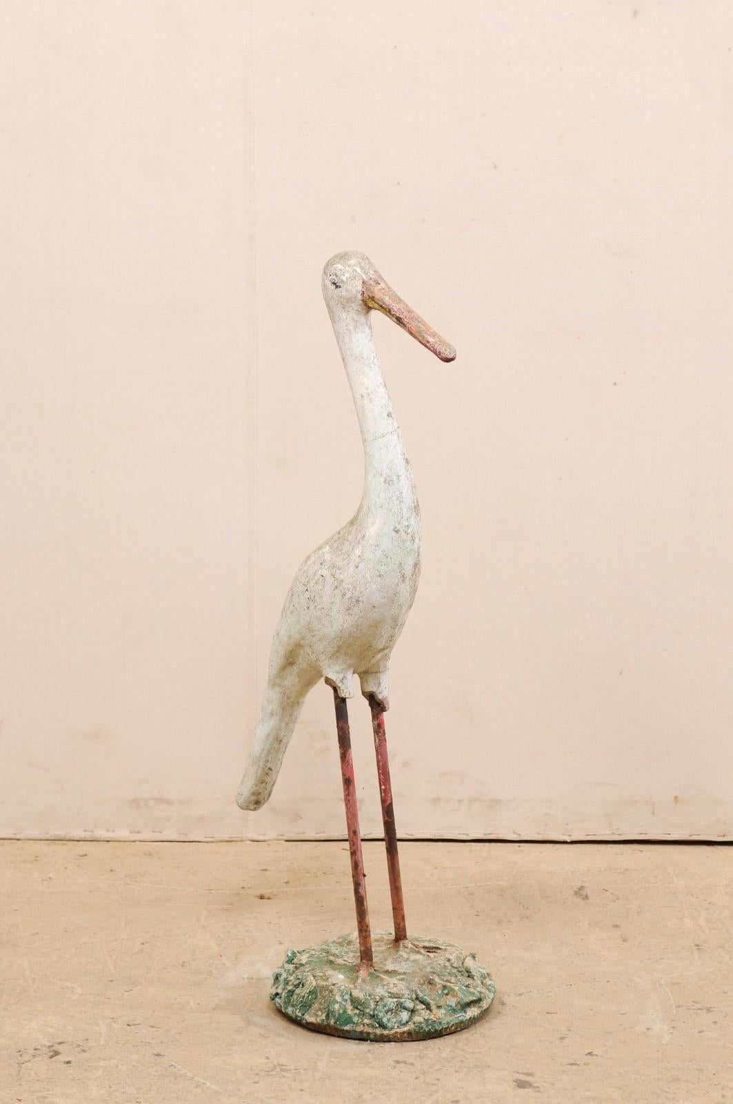 A French garden statue of a crane bird. This vintage statue from France, created in cast-stone, in the image of a crane, standing in with head forward and feet planted firmly in grass. This sculptural figure stands approximately 41