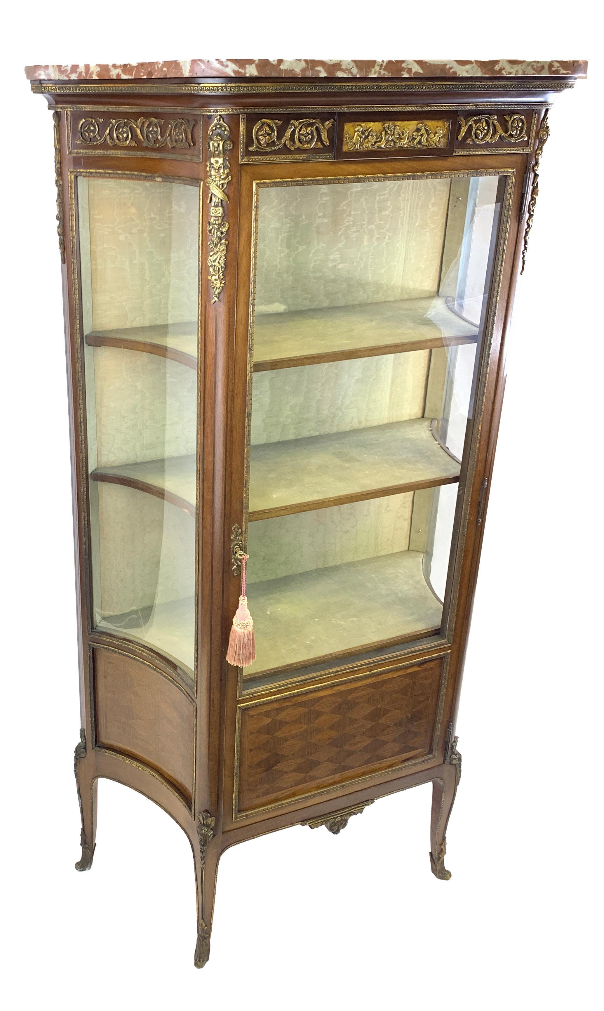 A French mahogany vitrine, circa 1900, marble top, the glazed door enclosing a silk-lined interior of three shelves and with glazed cavetto sides, having a central parquetry panel below, on scroll legs.
 