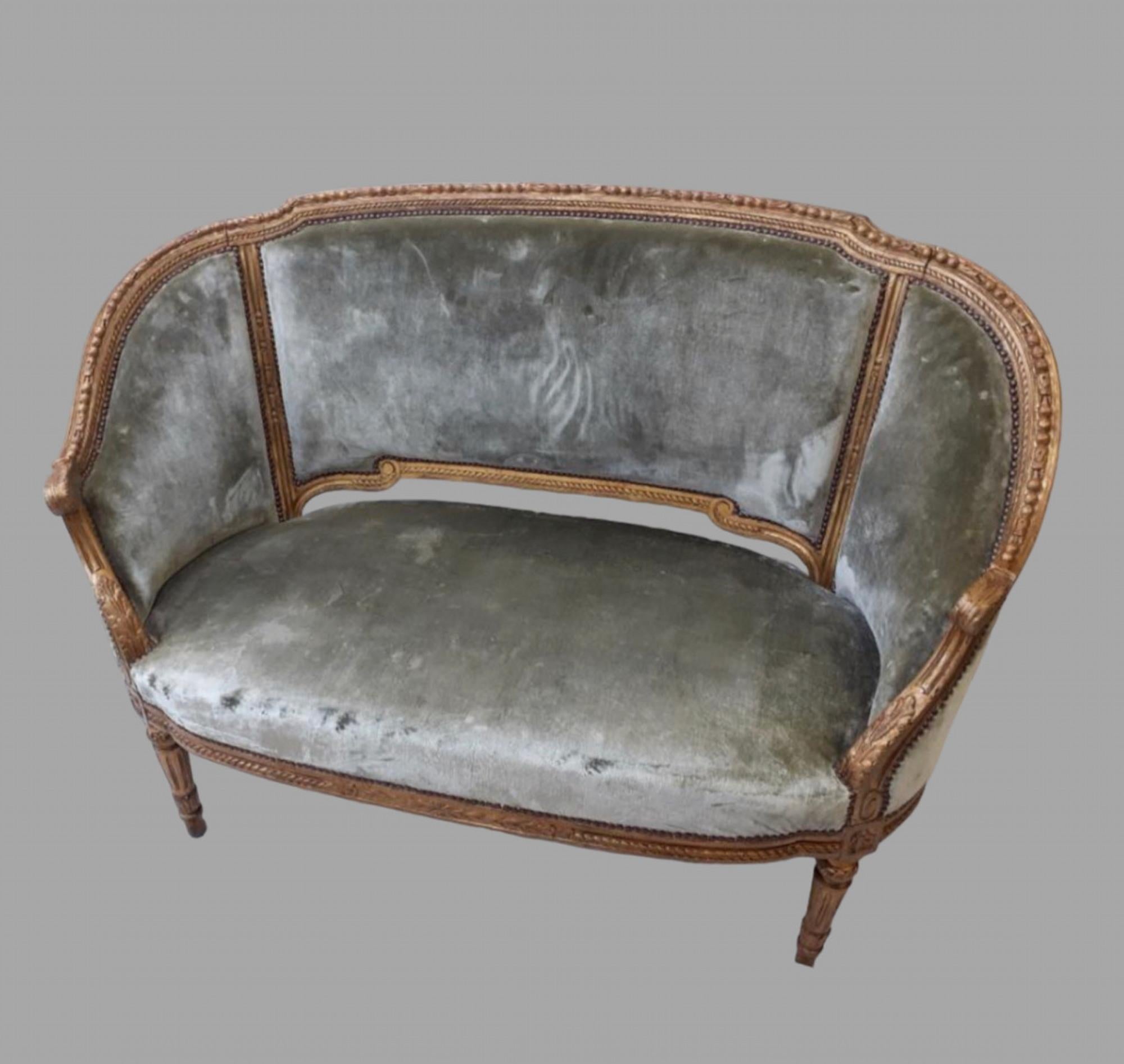An Early 20thc French Giltwood Canape covered in a silk original velvet with very small wear.. The frame has a continuous carved frieze ending in a leaf design terminating in tapered fluted legs. The bottom rail has a matching carving around it