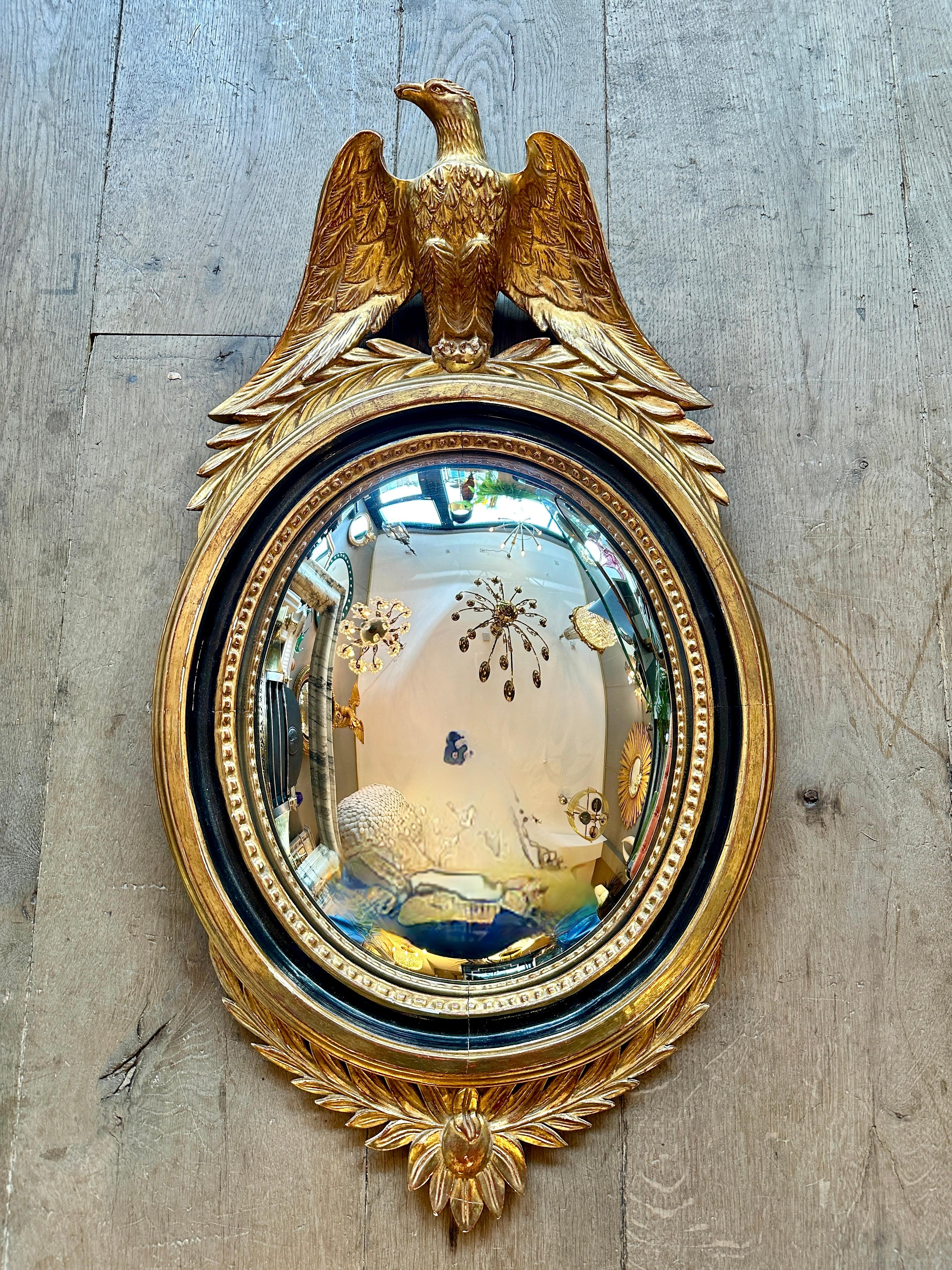 An Empire style late 19th c oval convex eagle crested giltwod mirror.  A well formed eagle with spread wings perched on laurels atop an oval conex mirror with plain frame with ebonized inner slip with beaded edge. The bottom also with laurel
