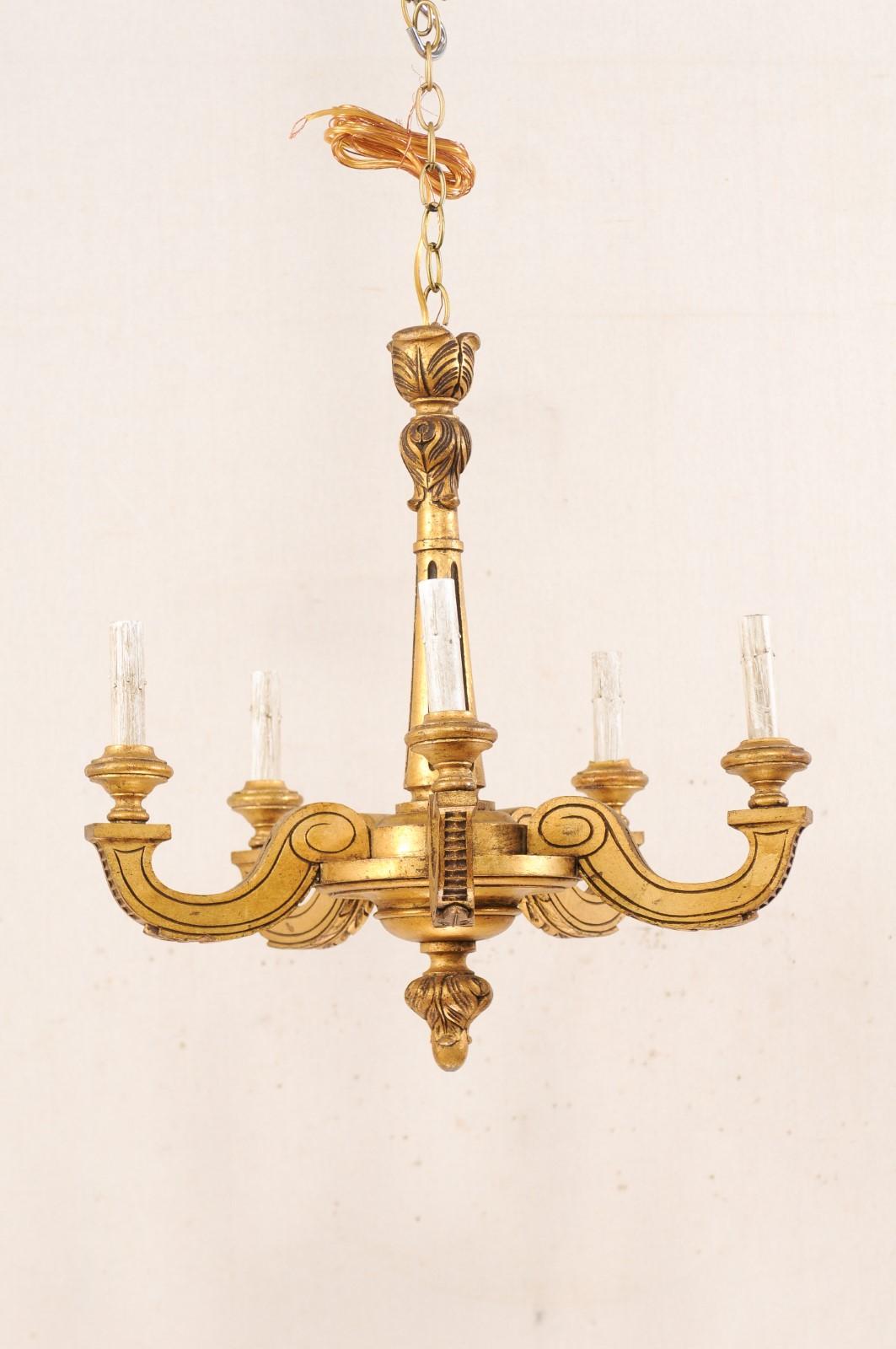 A French five-light gold tone carved-wood chandelier from the mid-20th century. This vintage chandelier from France features a rounded and fluted central column, which gradually widens towards the gallery, with leaf motif carvings at top, and