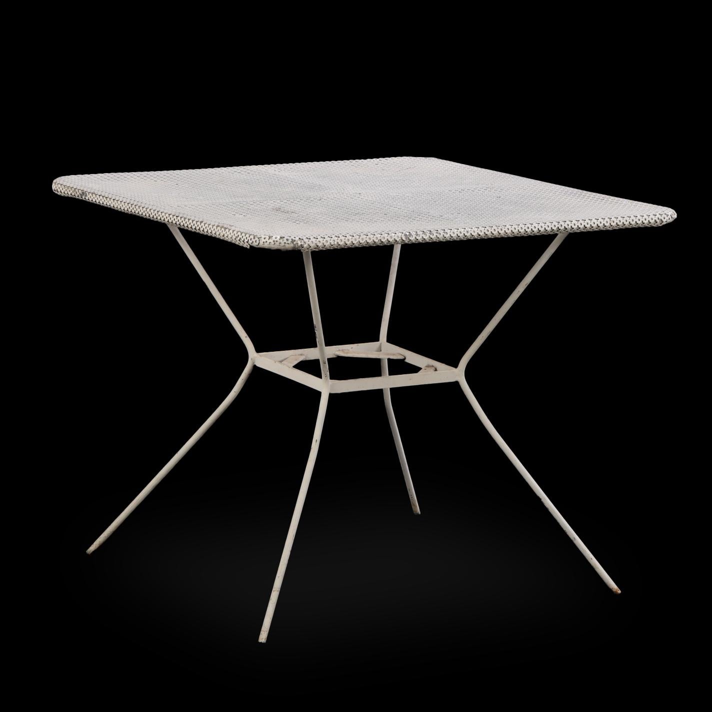 Il set comprende un tavolo quadrato e quattro sedie abbinate, ciascuna progettata con sottili telai in ferro tubolare e superfici perforate/mesh, che evocano lo spirito giocoso ma pratico dei mobili da giardino di Matégot della metà del secolo