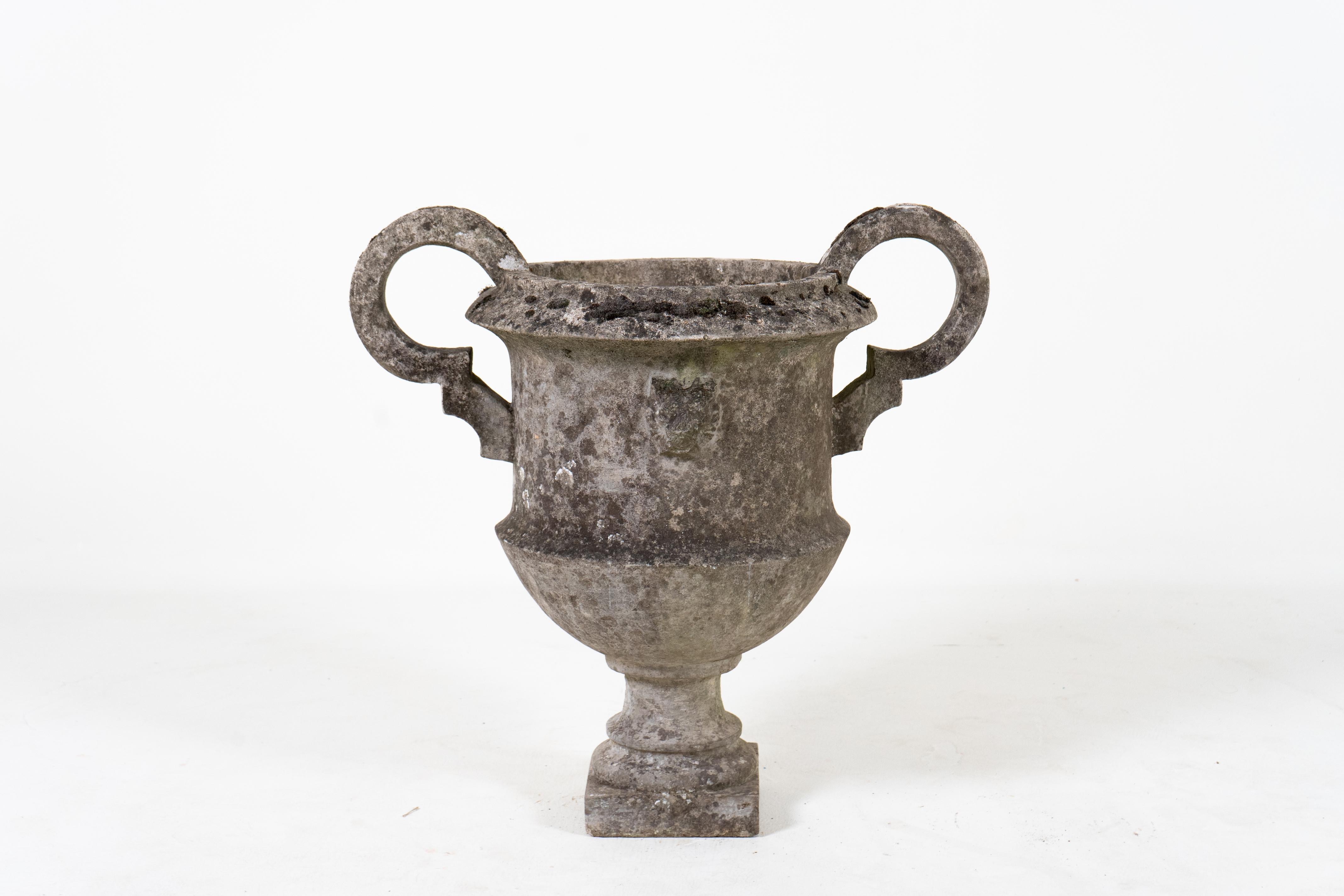 This large and well-preserved cement garden urn has large, rounded handles, a square pedestal base and embossed lions on its front and back. The piece was found in Normandie, France, where it has been in continuous outdoor use. The surface is richly