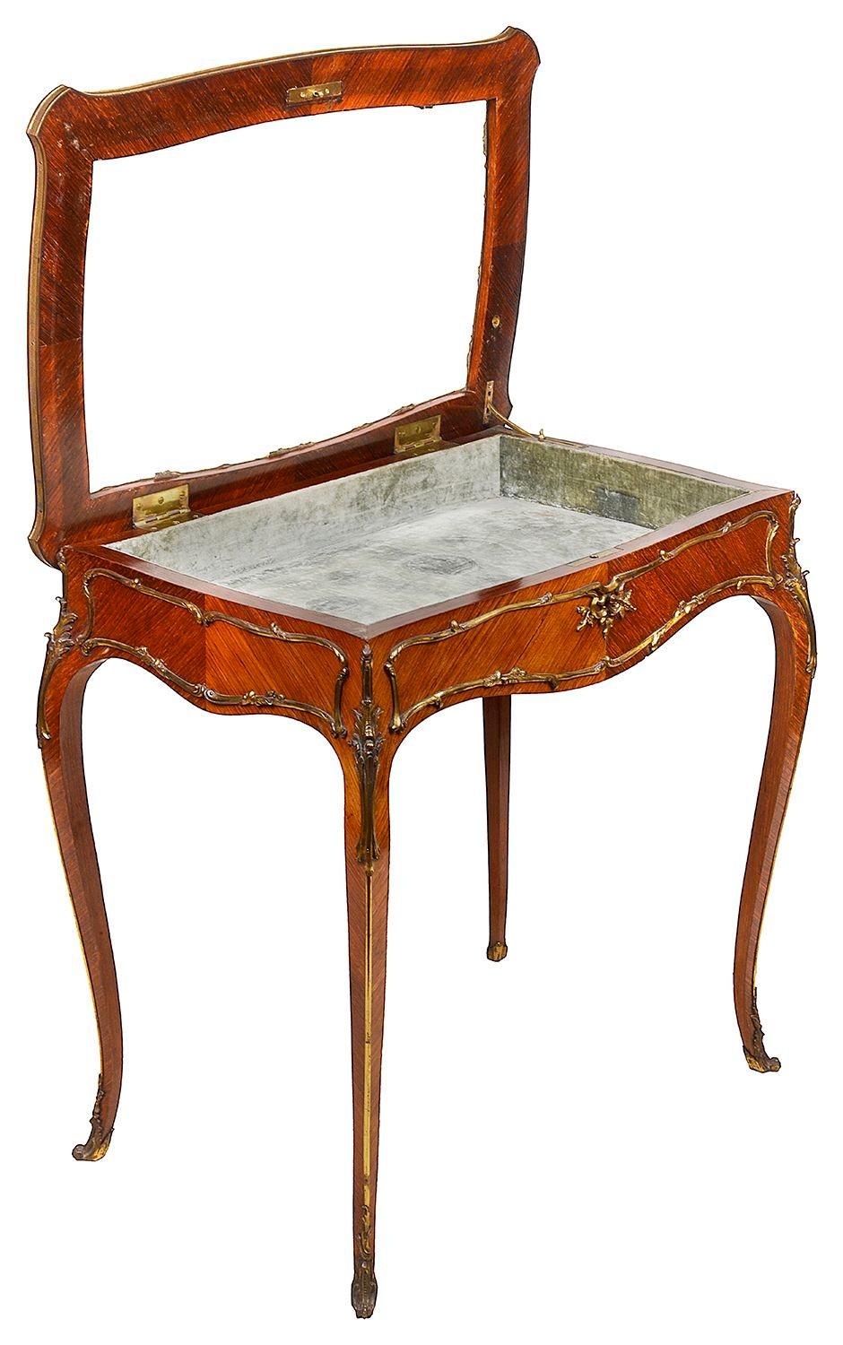 A French kingwood and ormolu-mounted bijouterie table, the shaped top with decorative ormolu moulding and shaped moulding framing the lid, the apron is shaped and framed by decorative ormolu mounts, the cabriole legs with decorative ormolu mounts