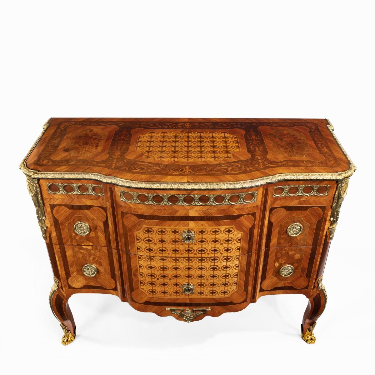A French kingwood marquetery commode, the shaped rectangular top inlaid with tulipwood, harewood and boxwood marquetry comprising a flowerhead trellis flanked by floral panels and within reserved foliate scroll borders and cross banding, above two