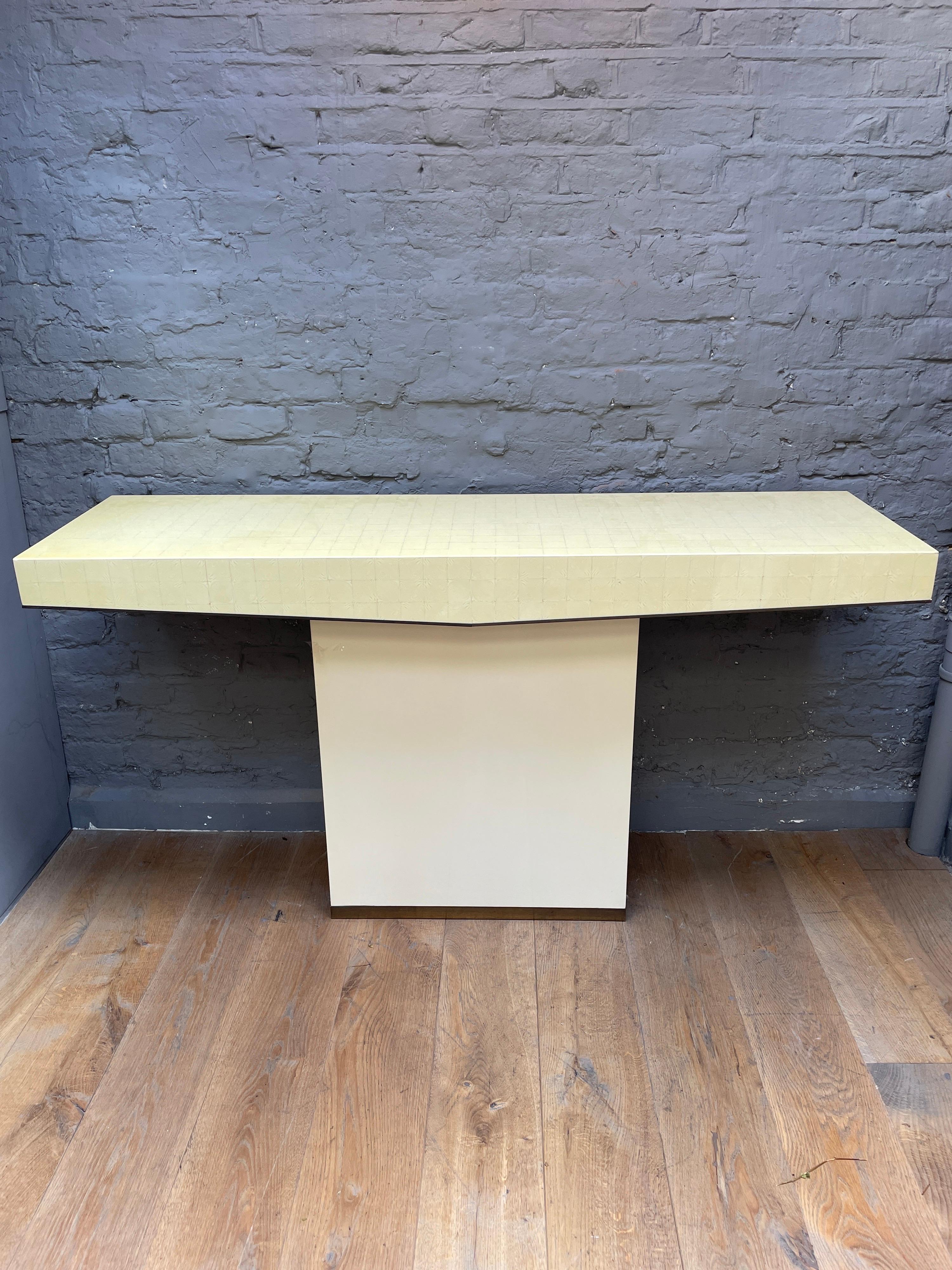 A large console table with cream lacquered base on brass plinth, the large top in lacquered segmented wood which shows the grain again edged in brass with the front panel tapering to a point. 
By J C Mahey 
France Circa 1970.